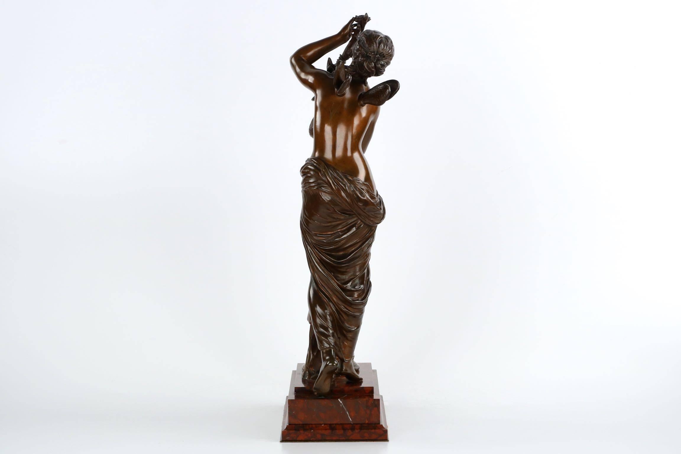An exquisite sculpture depicting “The Dawn” or “L’Aurore” by Mathurin Moreau, this moving work captures a timeless scene of a young nymph stepping up the stairs of this original rouge grotto marble base to greet the abundant flowers growing from a