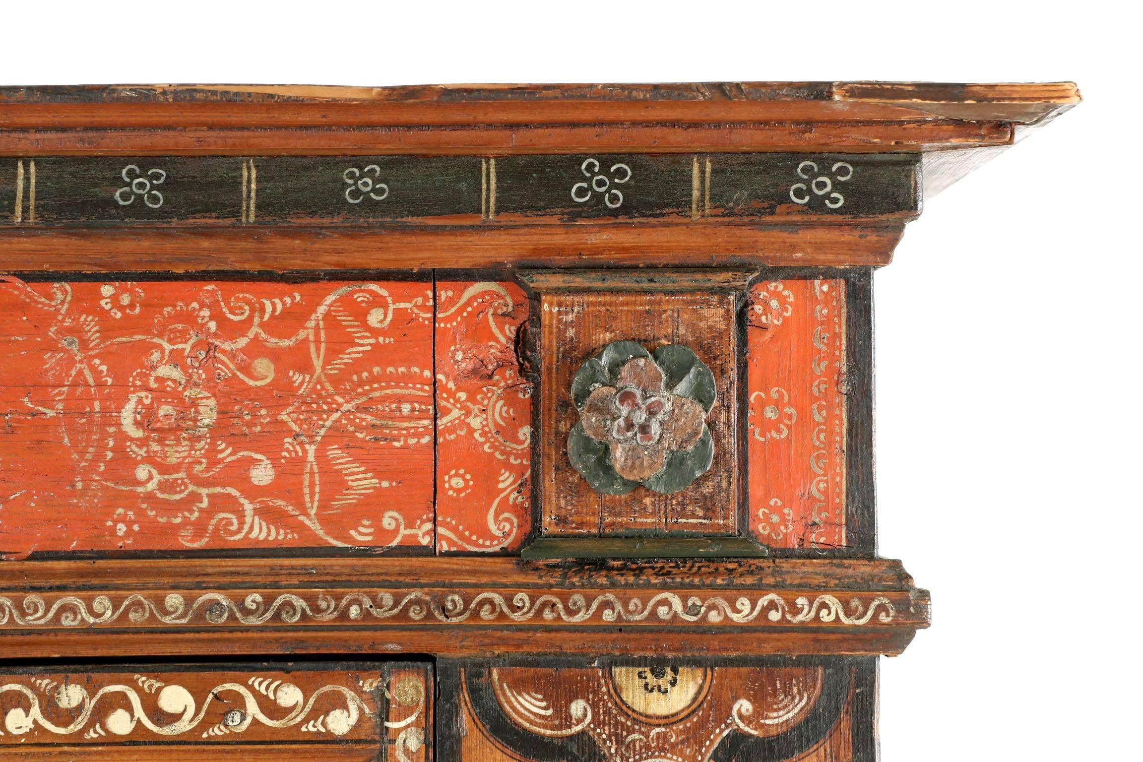 A most striking piece for its original grimy Folk Art painted surface, in particular the vivid display of symmetrical and yet wholly unique floral displays across the recessed panels in both doors. A burnt orange ground color allows the mellow