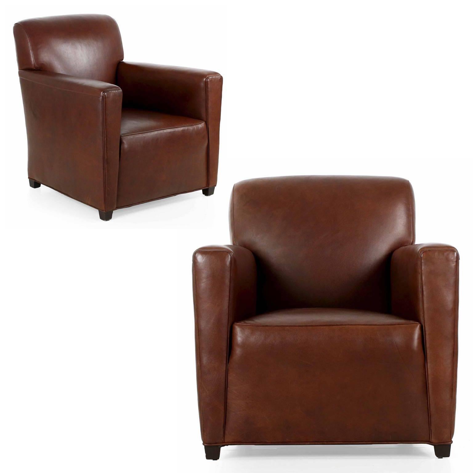 This pair of club chairs were designed with a nod to the elegance of the Art Deco era, with the attached back and seat presenting a unified, crisply tailored appearance. The tight back rests on a generous cube seat, defined by slight welts to accent
