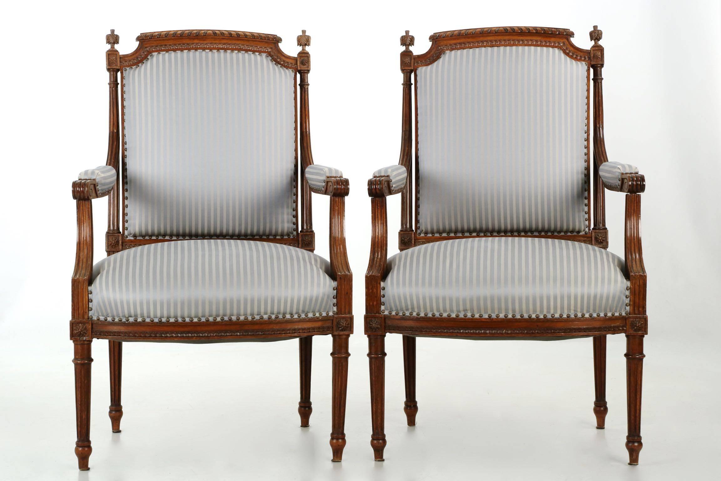 A most attractive pair of arm chairs in the Louis XVI taste crafted during the first quarter of the 20th century, both are carved of a dense walnut and retain early and beautifully patinated surfaces. The crest rail has a carved gadrooning across