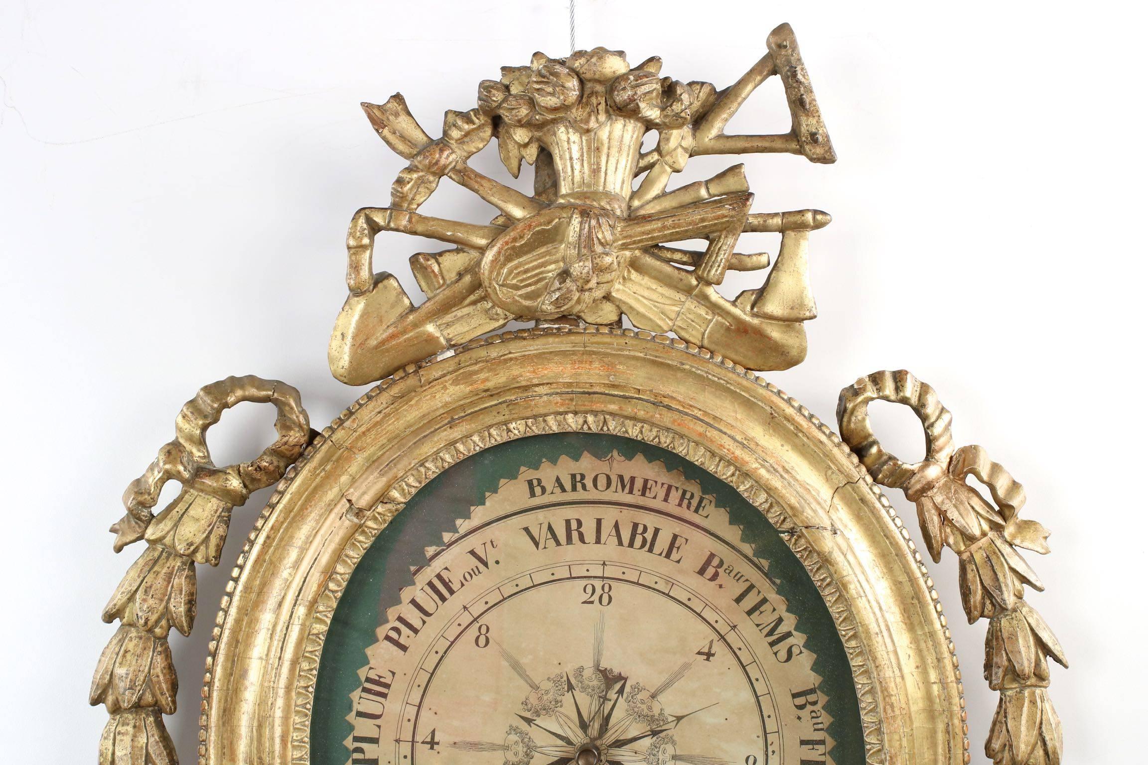 This lovely barometer is housed in a most active carved and gilded pine frame, the ovular body with simple molding from which sprout a large selection of harvest tools: two spades, a scythe, a rake and the bounty of the field sampled in a basket.
