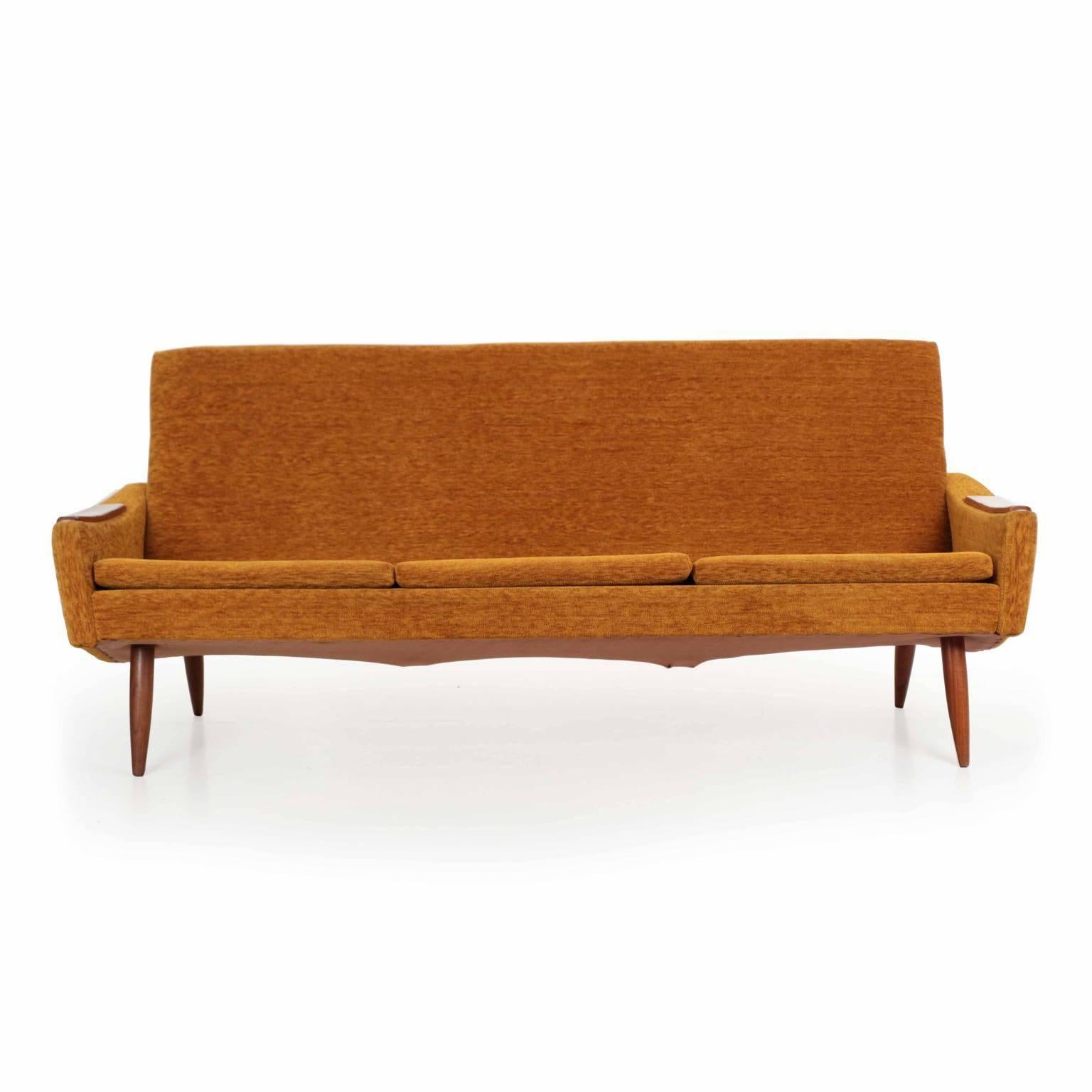 A very handsome and well designed piece, this sleek sofa was recovered at some point in a vintage orange covering that remains in excellent overall condition. A distinct angularity is found in the curvature of the back and the inward cant of the