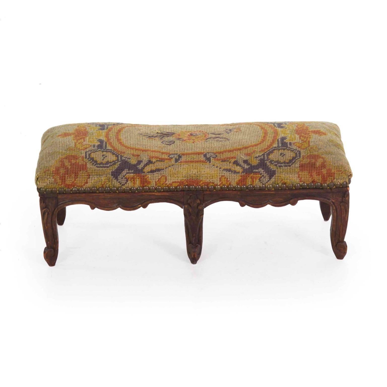A gorgeous little early footstool of unusually diminutive proportions, this is an interesting accent piece with such a rich old surface. Retaining the early hand-stitched needlepoint covering surrounded by brass tacking, the fruitwood frame is