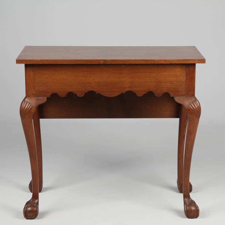 A table that is intended for display against the wall with it's exposed apron facing out, the front two legs are highlighted with beautiful raised shells while the rear legs are unadorned. The boards have a beautiful flowing grain, the top boards