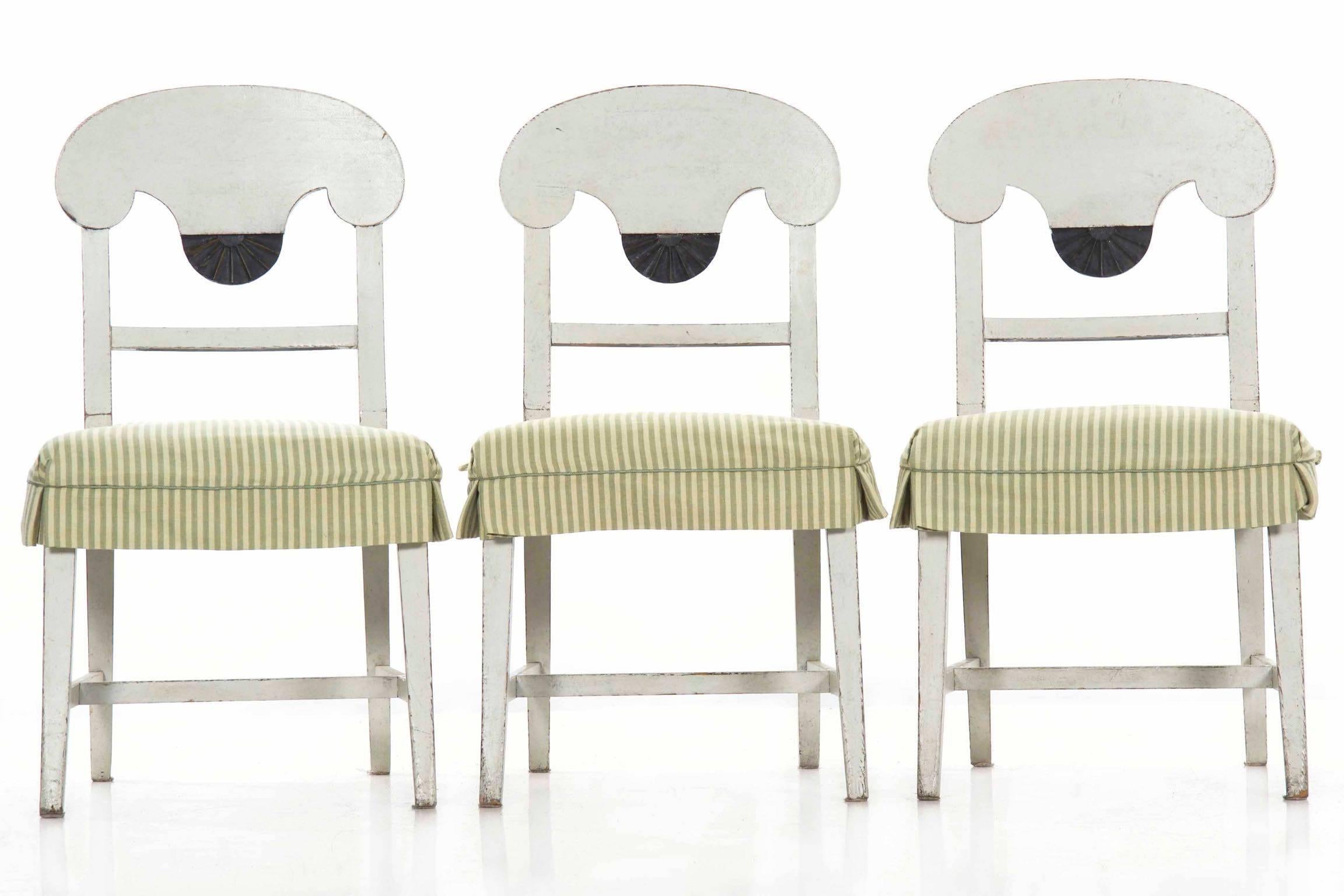 This delightful set of six chairs crafted in the Swedish Gustavian taste are finished in a gorgeous and nicely worn mottled white paint. The back of each chair is clearly influenced by the Empire forms of the early 19th century, the dramatic curving