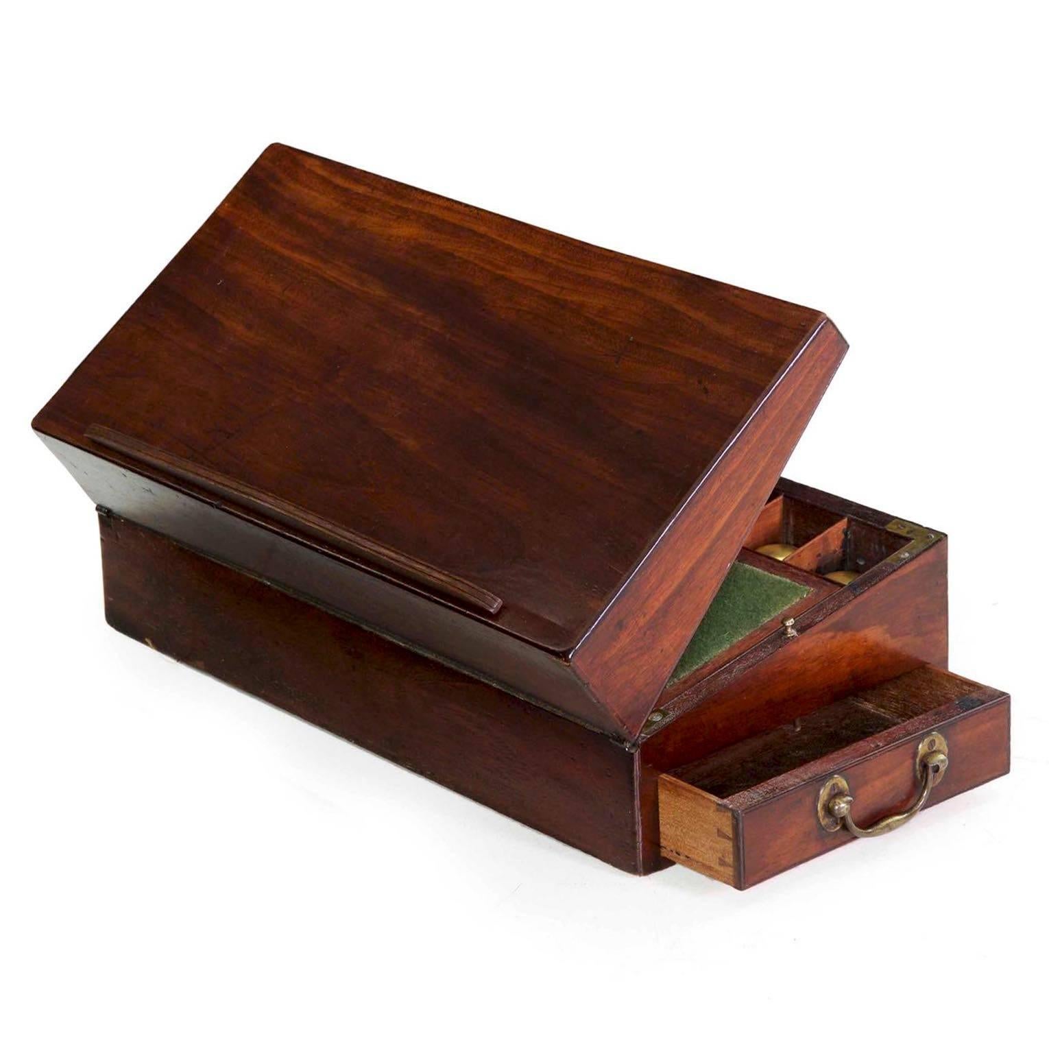 A rare find in this condition and with this degree of originality throughout, this fine mahogany writing slope is austere and simple in form. Original heavy brass carrying handles flank the box, one acting also as the draw for a small drawer; this