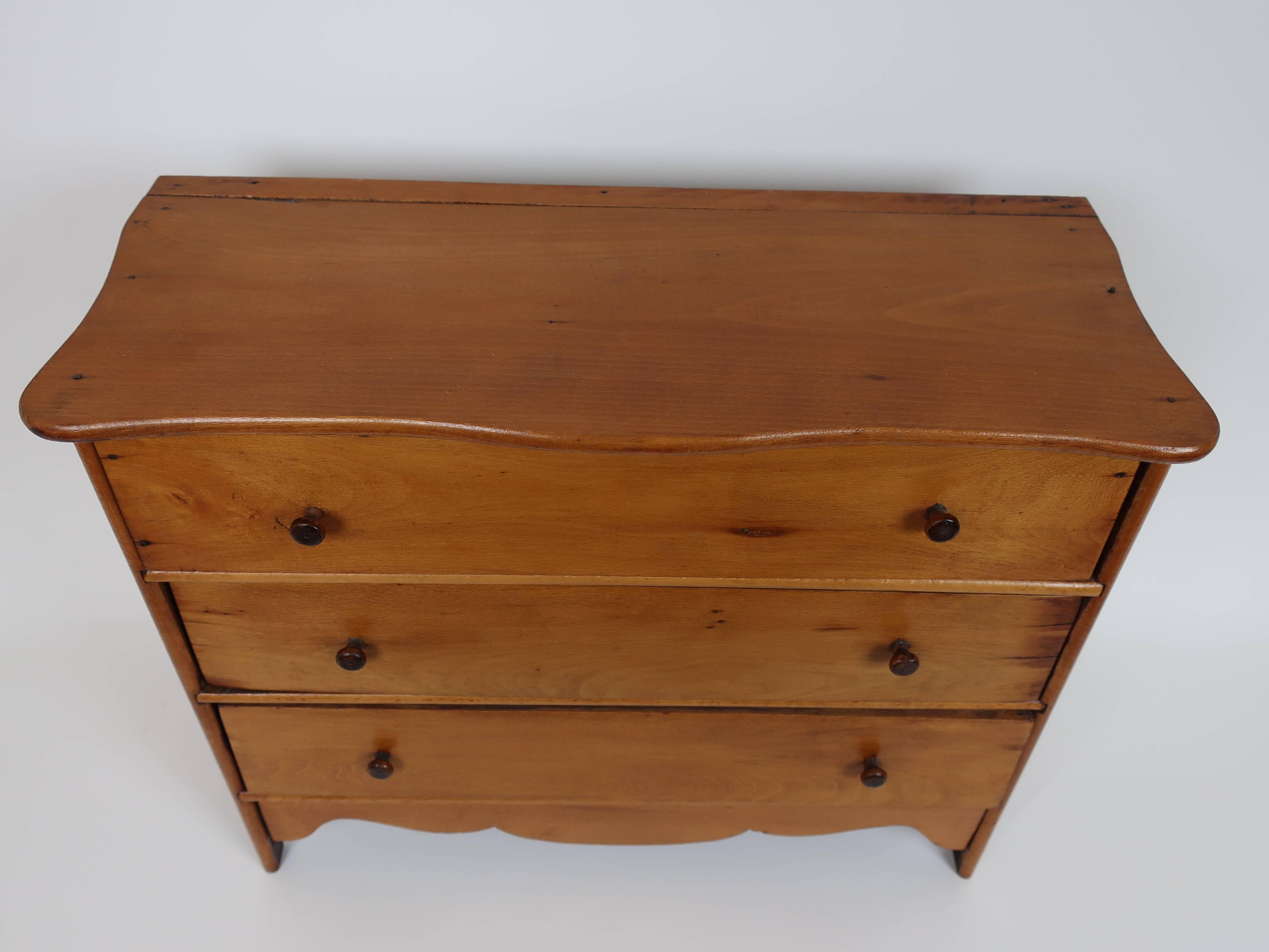 Miniature pine chest from New England with shaped top, delicate turned button pulls and scalloped apron. The finish is original with a lovely patina and the scale is delightful.