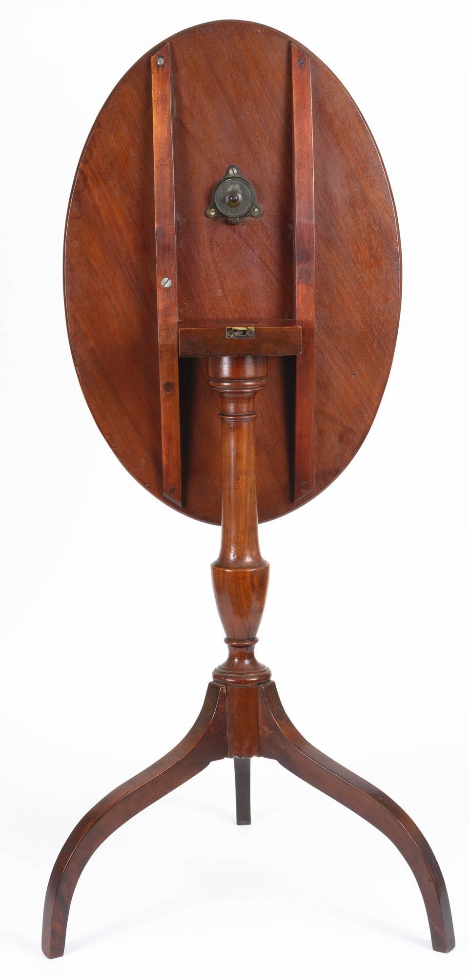 American Hepplewhite tilt-top candle stand with oval top of figured wood. The column has urn and concave turnings with delicate curve detail at the base. The splayed legs are well proportioned. The parts of the table are mortised joinery.
The