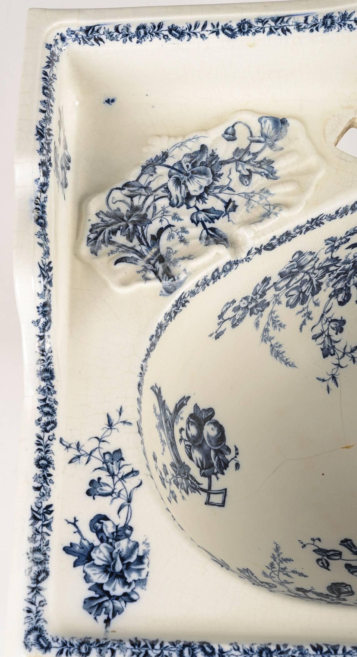 Blue and white transfer pattern of garland and flowers in the style of Berain, decorate this porcelain lavatory sink. The bowl has two soap 
