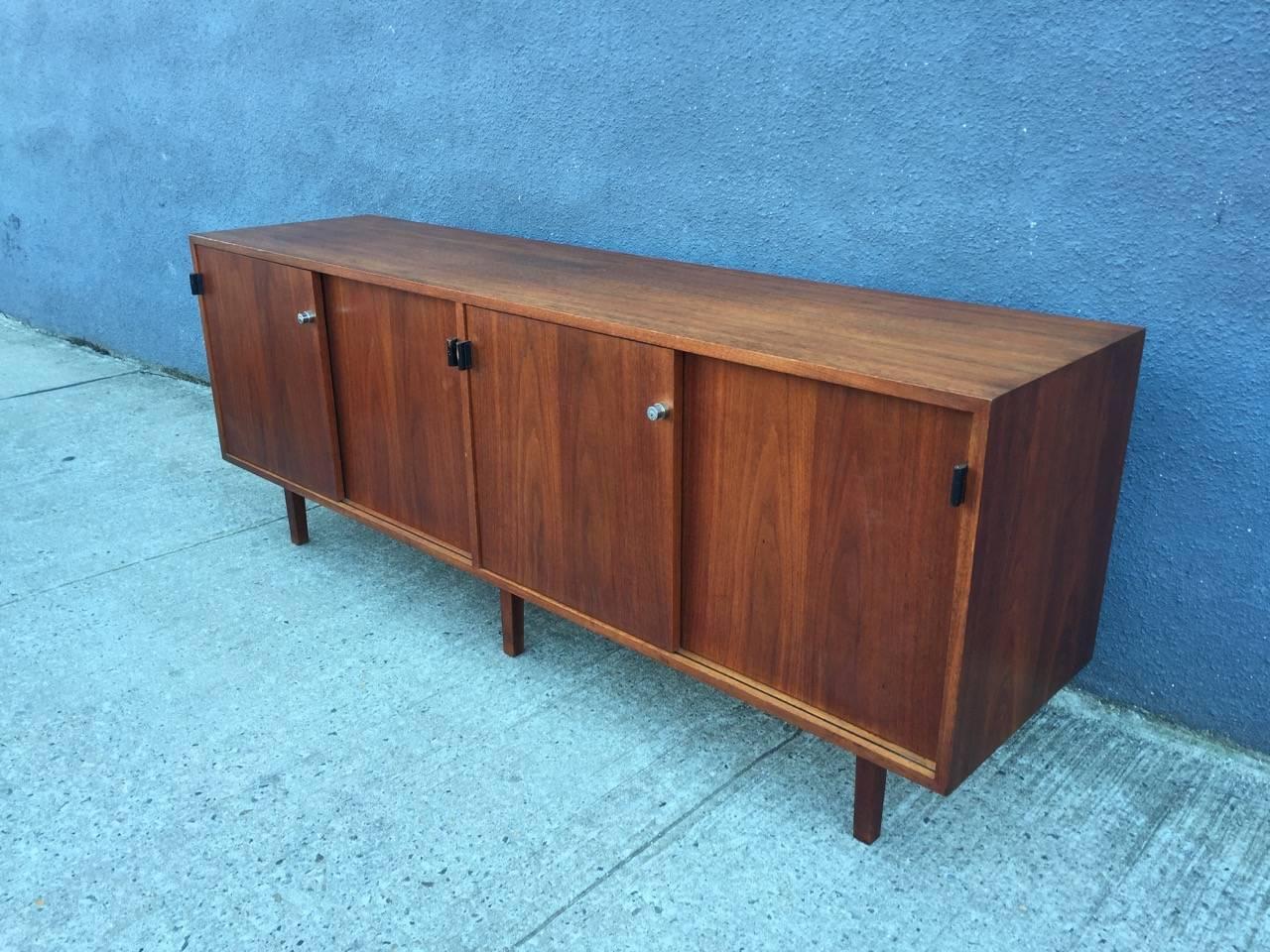 For your consideration is a rare walnut cased credenza designed by Florence Knoll for Knoll, featuring leather pulls and walnut legs. This is an early version of Florence Knoll’s iconic storage unit, with the feet supporting the casing from