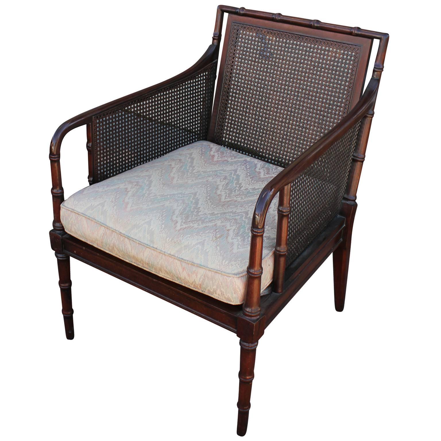Elegant pair of Regency style lounge chairs. Faux bamboo frame has simple curved lines. Seat back and arms are covered in cane. Seats are upholstered in a vintage chevron fabric which needs to be updated. The chairs are very well constructed and