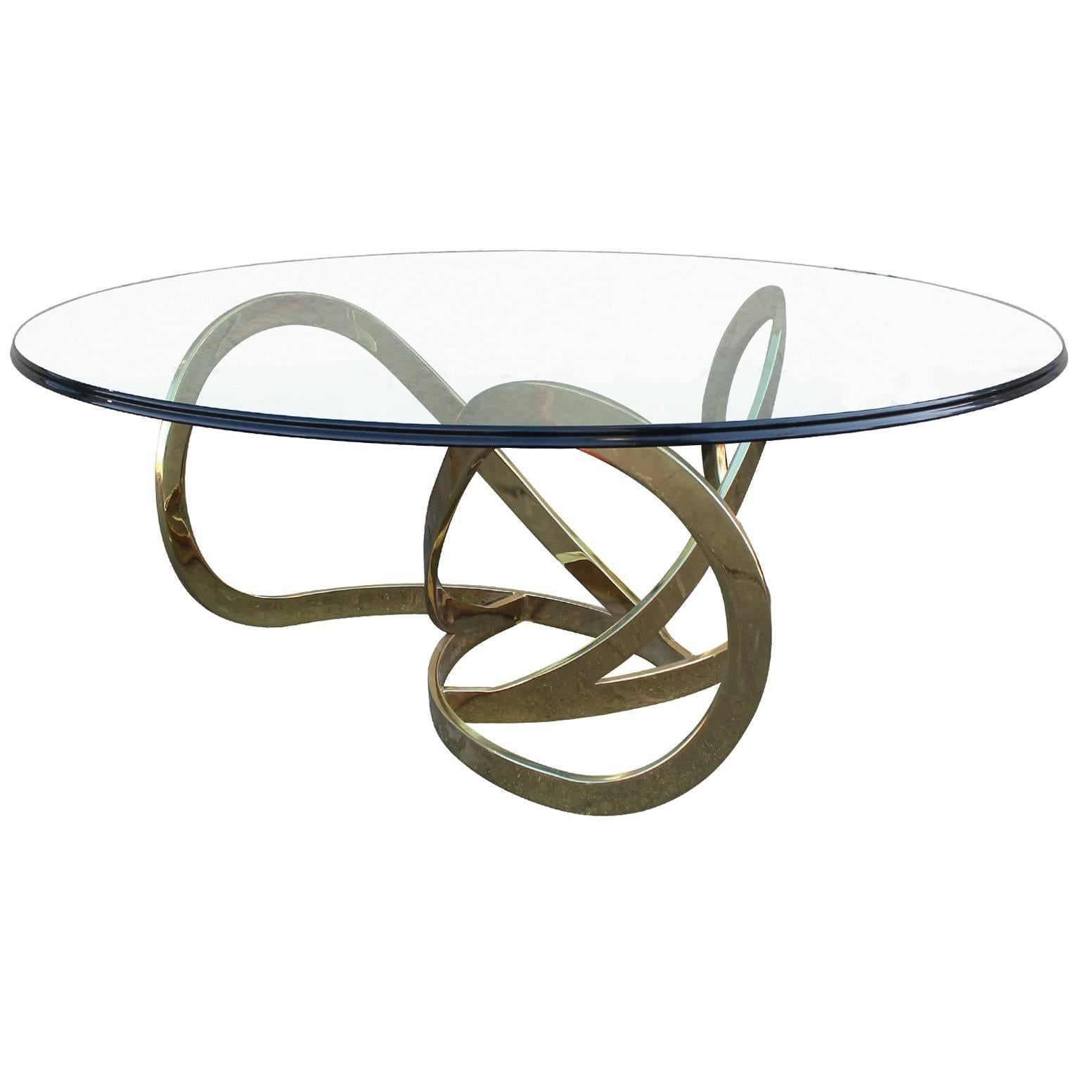 Glamorous round coffee table in the style of Milo Baughman. Thick cut-glass top rests upon a shiny brass base.
