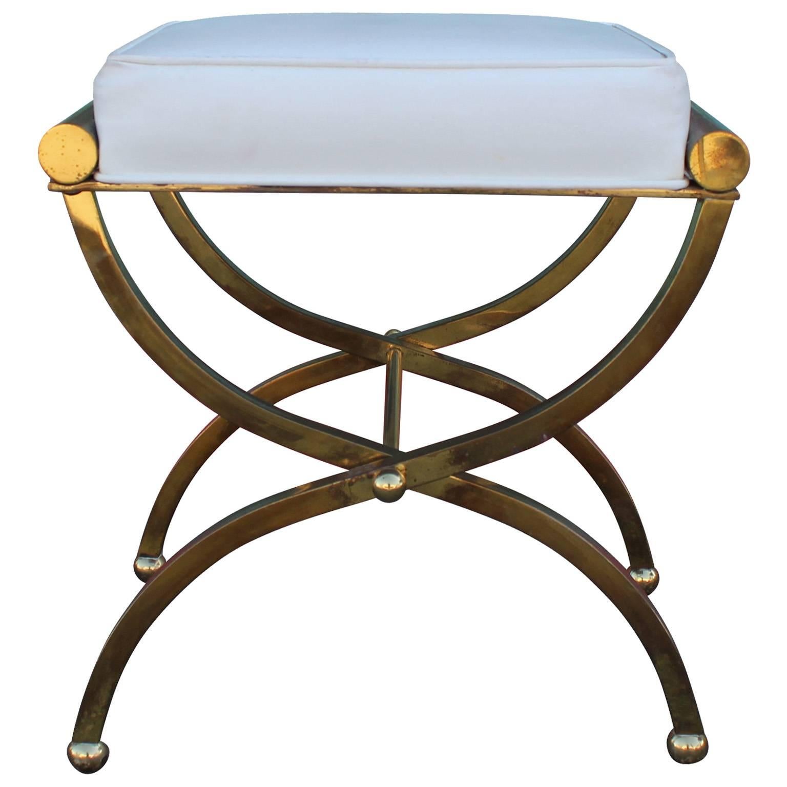 Lovely X-base stool. Curved X-base is in solid brass with an excellent patina. Seat is upholstered in a white faux leather and should be reupholstered.