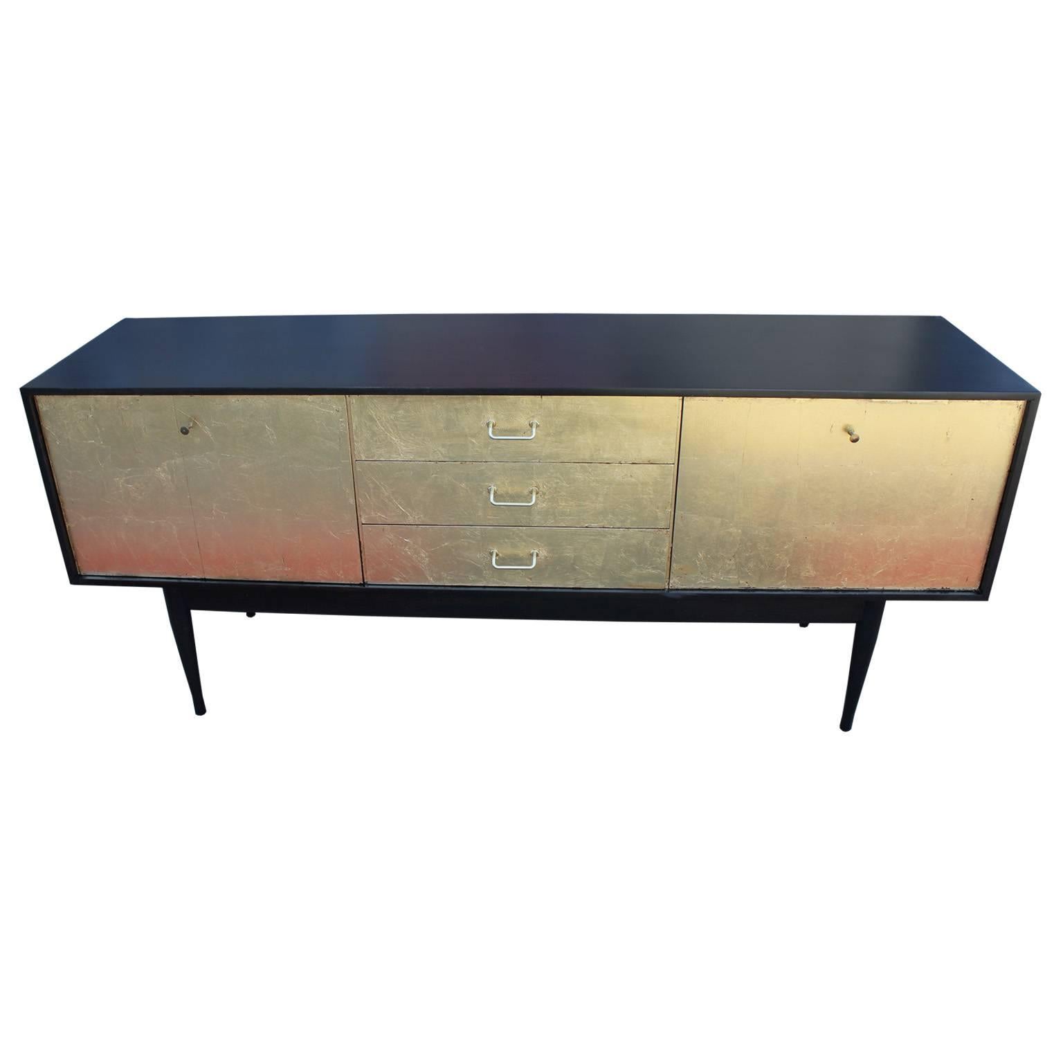 Glamorous sideboard freshly finished restored in an ebonized stained shell with a bold gold leafed front. The left door is a bi-fold while right door drops open a serving platform. Three drawers finish off the center. The sideboard is stunning from