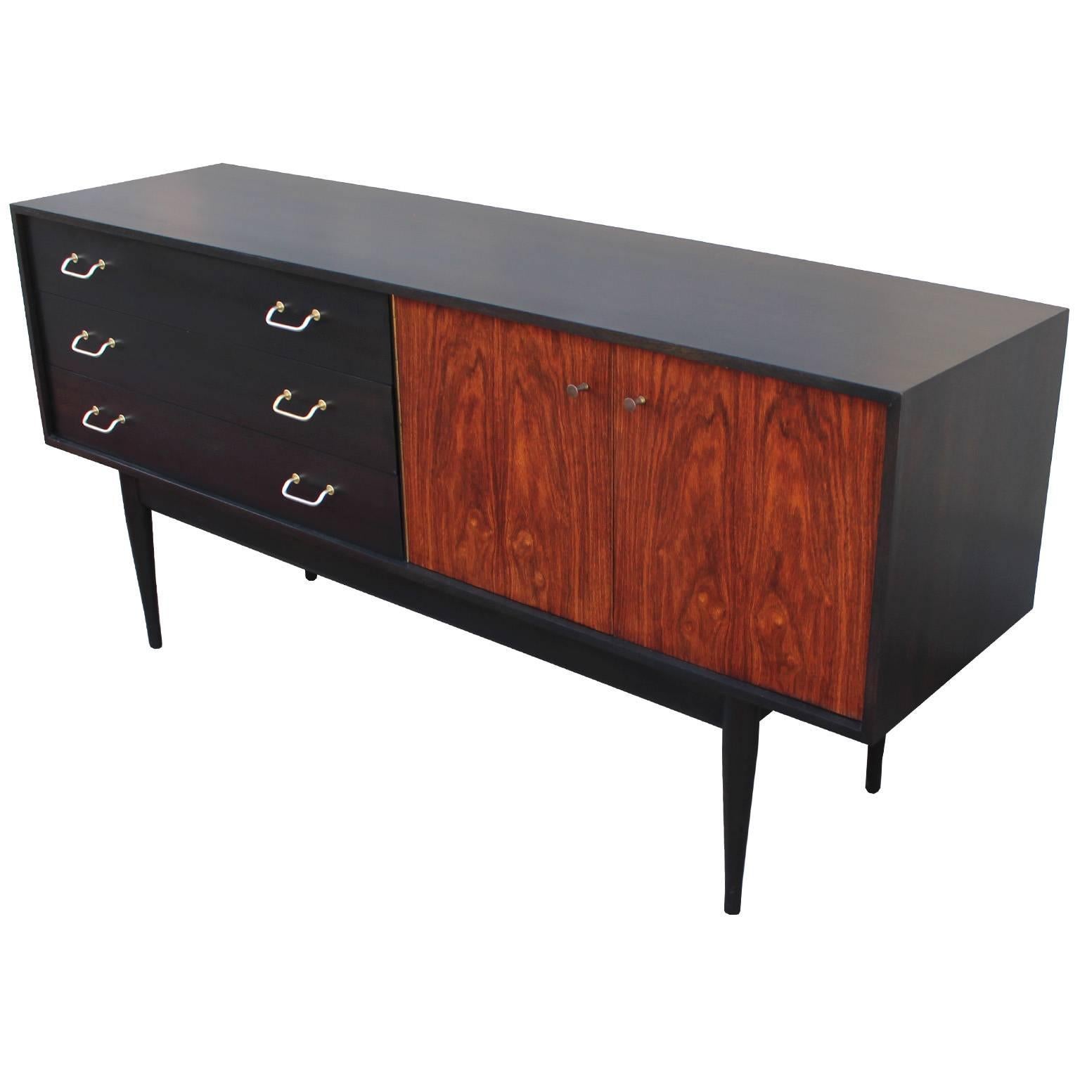 Great two-toned sideboard with a stunning lively teak front. The shell has been finished in a deep ebony stain finished off with brass tone aluminum handles. The doors have small brass pulls the compliment well. A wonderful statement piece.