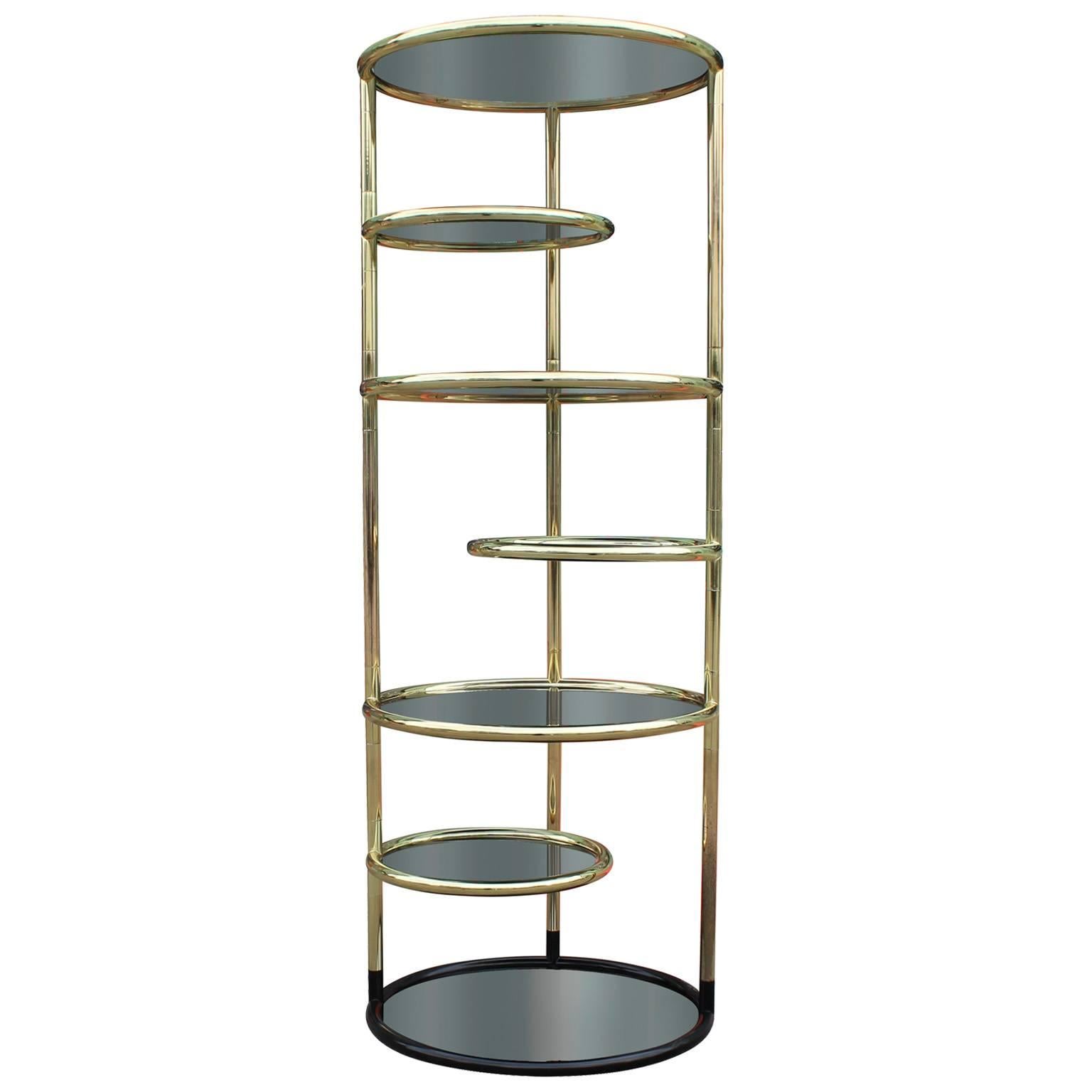 Eye catching etagere or display in tubular brass and smoked glass. Three smaller alternating shelves swivel 360 degrees. In the style of DIA. The bottom section is black lacquer.