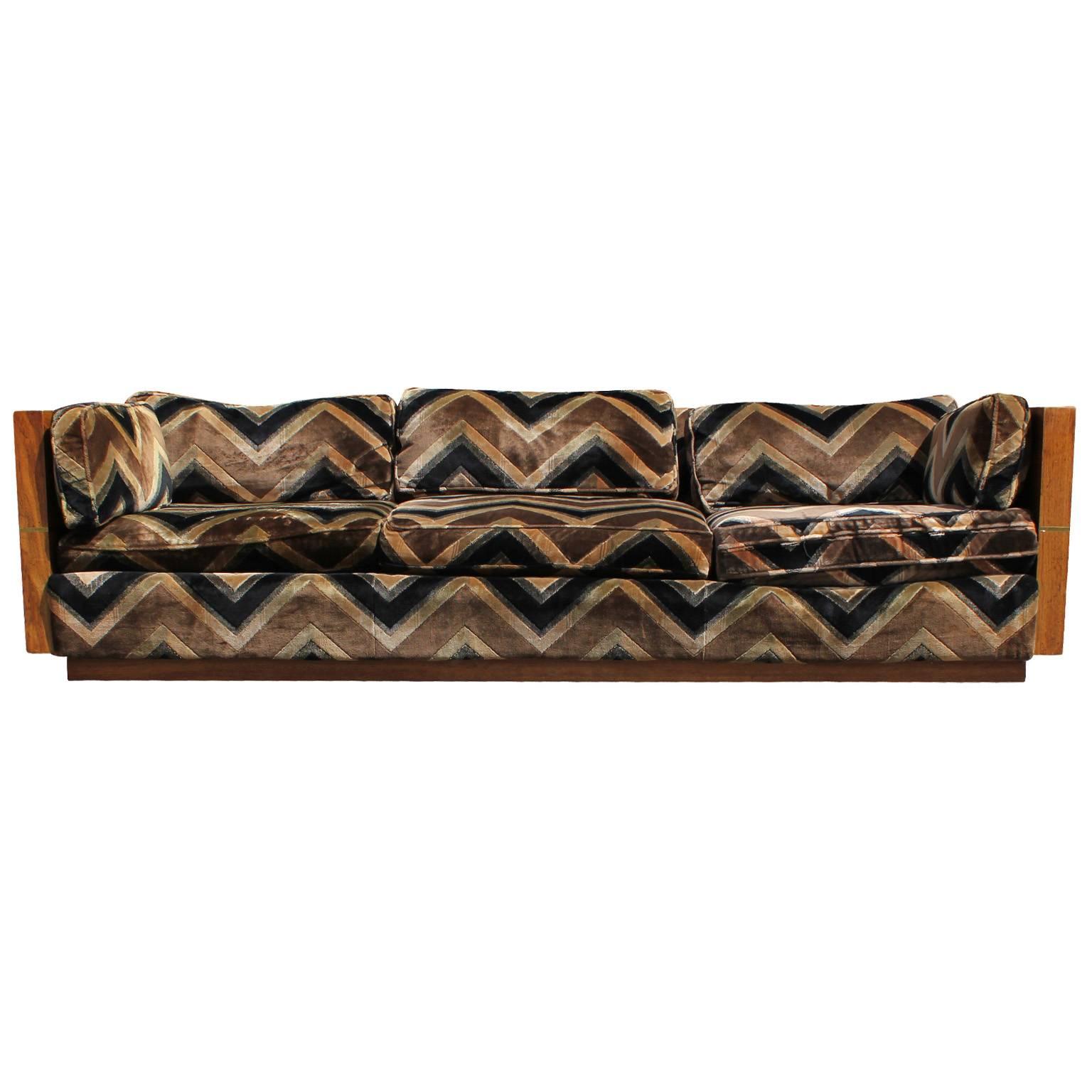 Incredible sofa attributed to Milo Baughman. Wood case has a striking grain and a brass strip grid overlay. Brass grid is peeling in one area and is easily removed. Upholstered in original chevron patterned velvet which needs updating. Matching love