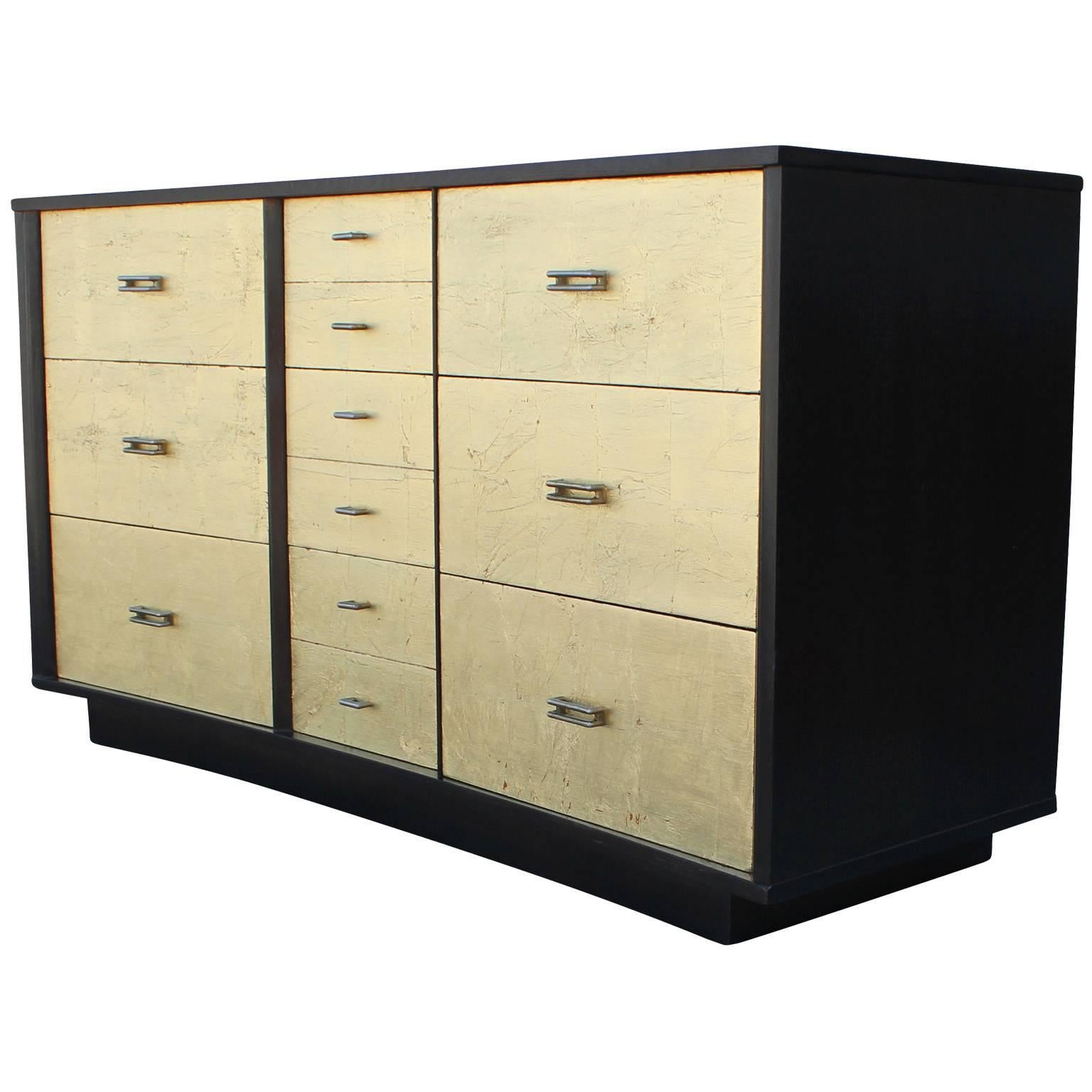 Ultra luxe dresser finished in gold leaf and ebony stain. Dresser has a subtle bowed shape. Six large drawers and three smaller drawers provide excellent storage. Dresser would be perfect in a Mid-Century, Hollywood Regency, or modern interior.