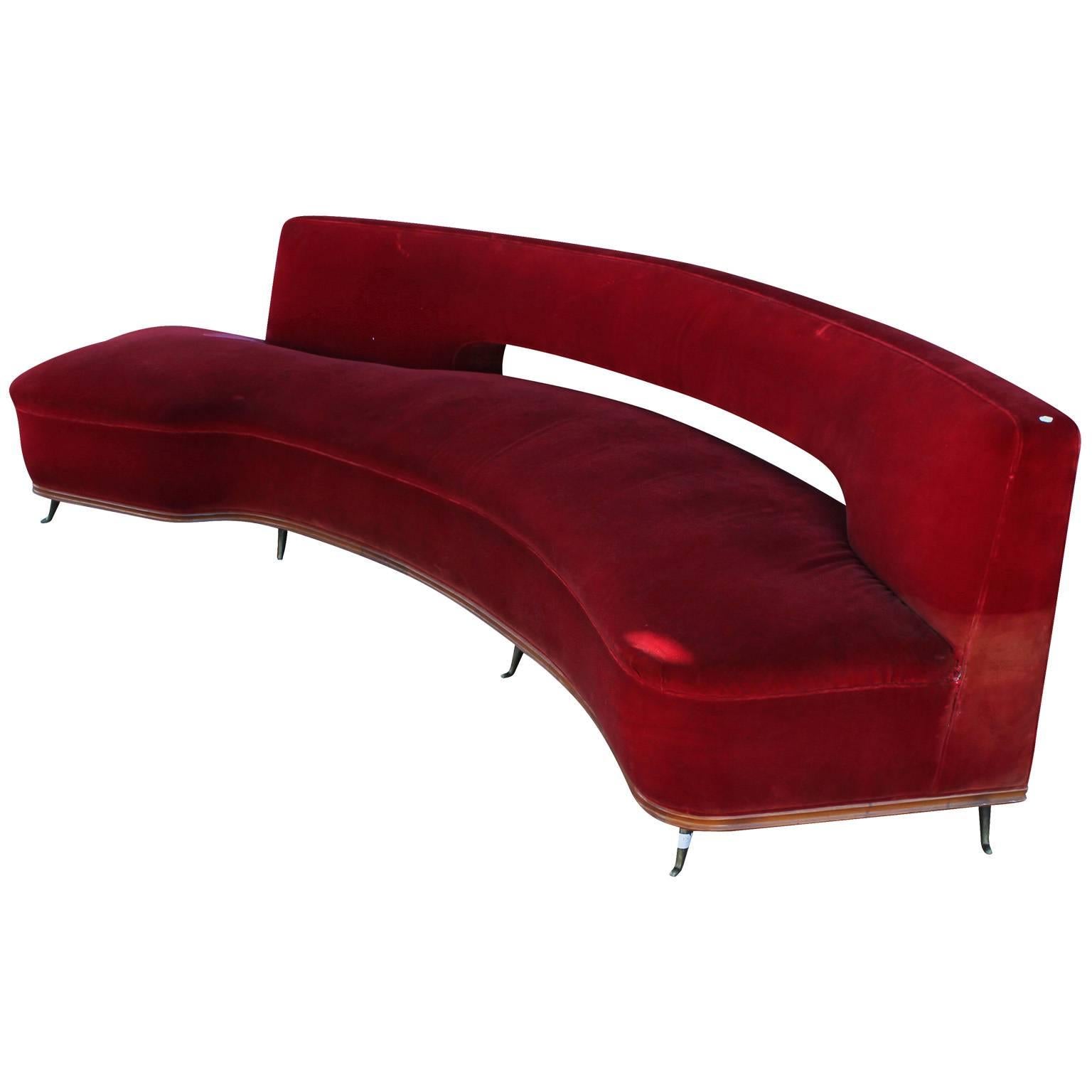 Glamorous and sculotural curved sofa by Federico Munari. Sofa has incredible curved lines and negative space. Sofa is trimmed with a carved wood base and six delicate brass legs in front and four tapered wood legs in back. Upholstered in red velvet