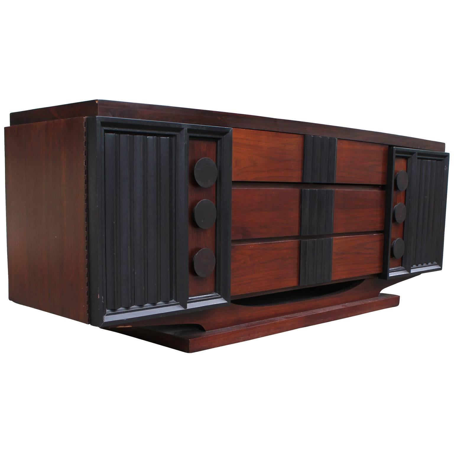 Fabulous sideboard or dresser with tons of visual interest. Sideboard is finished in a two tone walnut and ebony. All sculptural components are in ebony. Cabinet doors on either side open to reveal drawers. Three center drawers provide additional