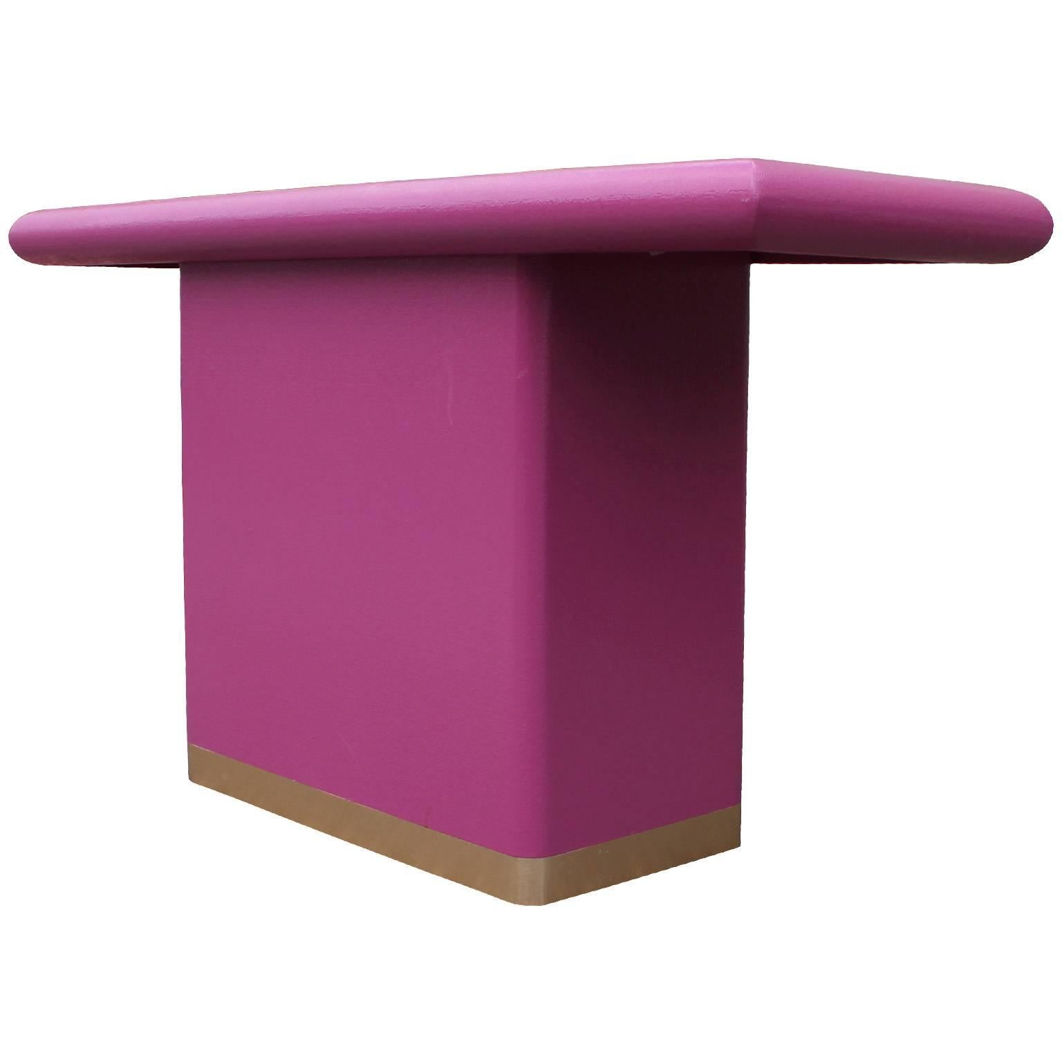 Glamorous console table in the style of Karl Springer. Console table is wrapped in raffia which has been lacquered in magenta. A brushed brass band finishes the piece.