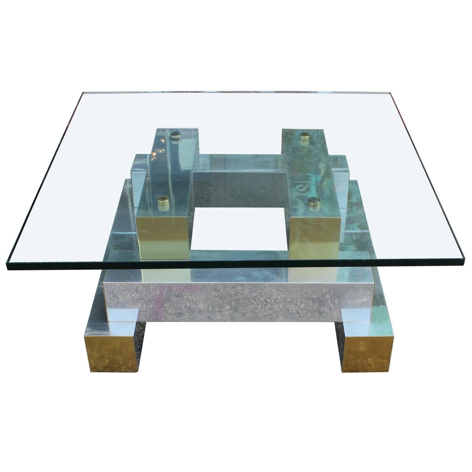 Bold glass topped brutalist coffee table. Chunky base is polished aluminum with brass accents. Topped with a thick piece of square cut glass. The perfect addition to a modern, Mid-Century, Brutalist, or Hollywood regency style space. In the style of