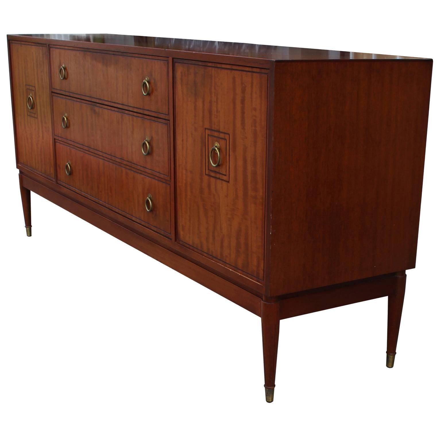 Elegant English sideboard or credenza. Sideboard has clean lines with a touch of traditional detailing making a perfect transitional of Hollywood Regency piece. Shiny brass ring pulls and caps finish the piece. Two cabinet doors open to a single