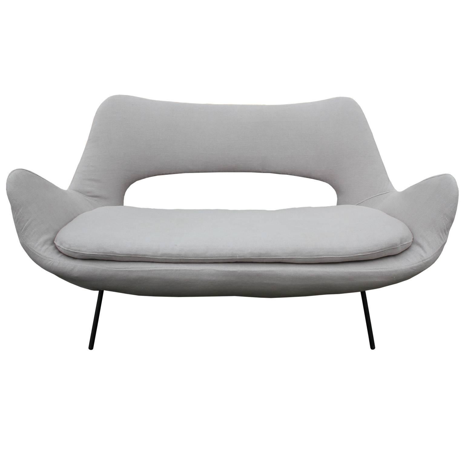 Incredible loveseat or small sofa. Loveseat has wonderful sculptural lines and negative space reminiscent of Arne Jacobsen. Freshly upholstered in a hand-stitched grey linen. Finished with tubular black metal legs. Perfect in a modern, Scandinavian,