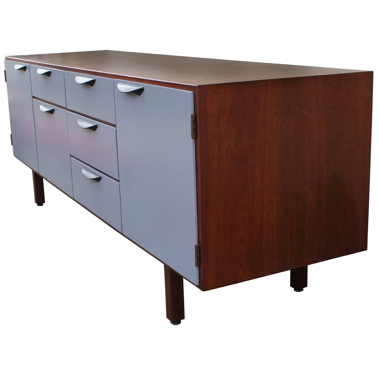 Excellent sideboard or credenza designed by Jens Risom. Drawers are finished in a smooth grey lacquer while the case is finished in a medium walnut. Walnut has beautiful graining. Aluminum hinges and pulls. Pulls are finished in a black aluminum