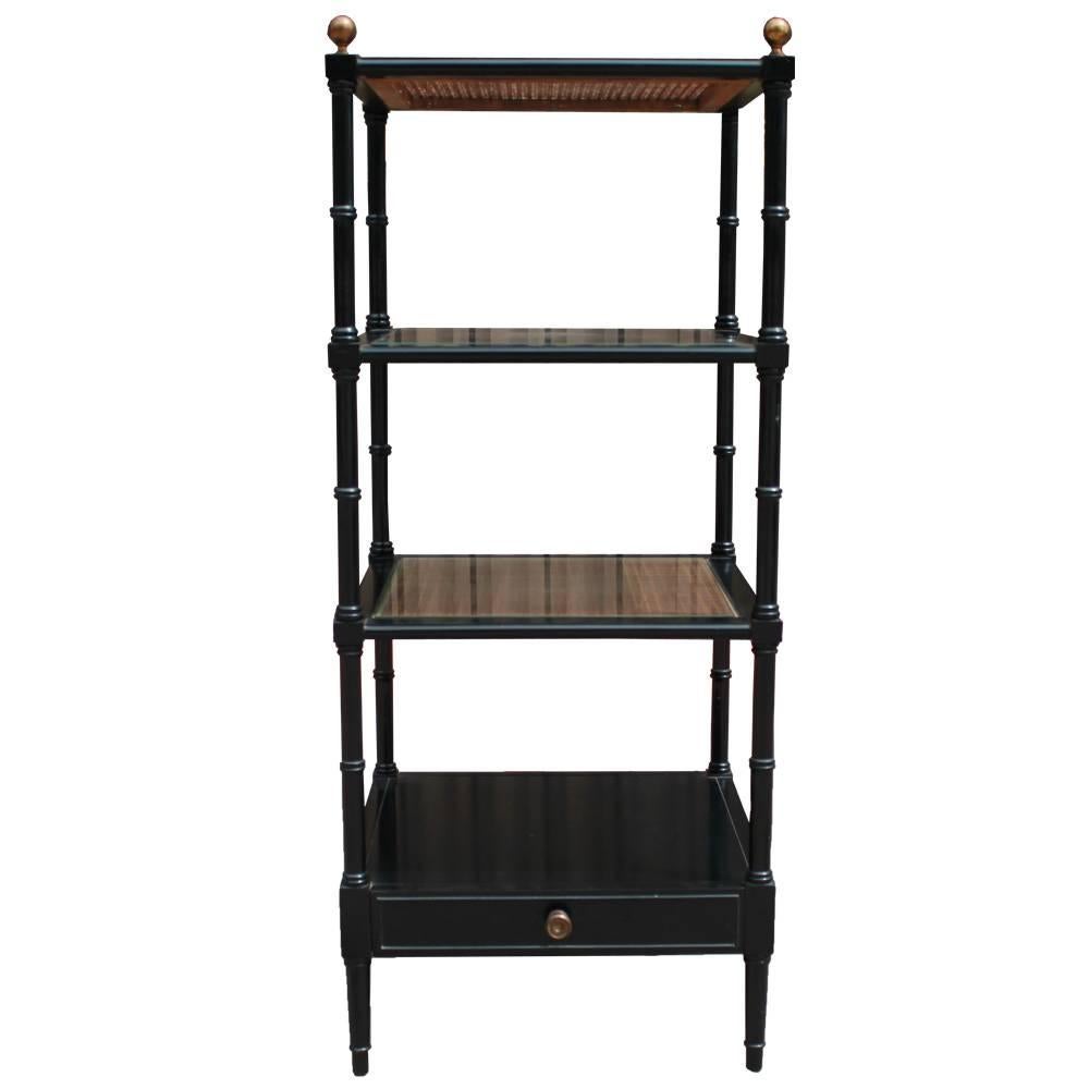 Charming etagere finished in black lacquer with gold accents. Three glass topped rattan shelves. A single drawer provides additional storage. Perfect for showcasing books and objects d'art.
