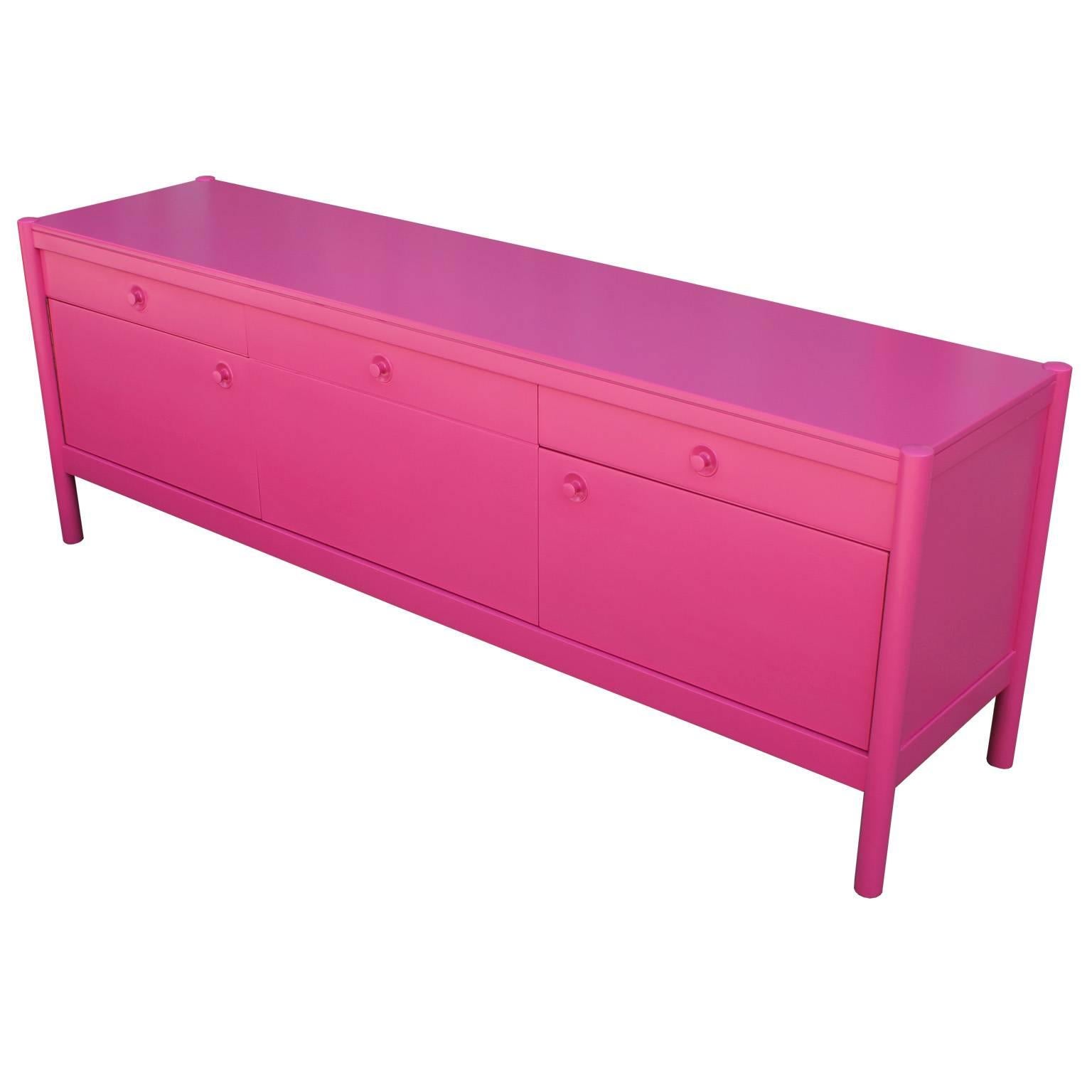 Fabulous credenza or sideboard fully finished in an ultra smooth hot pink lacquer. Left door reveals open cabinet space. Middle door drops down to reveal a single shelf. Right door opens to a single shelf. Two drawers provide additional storage, one