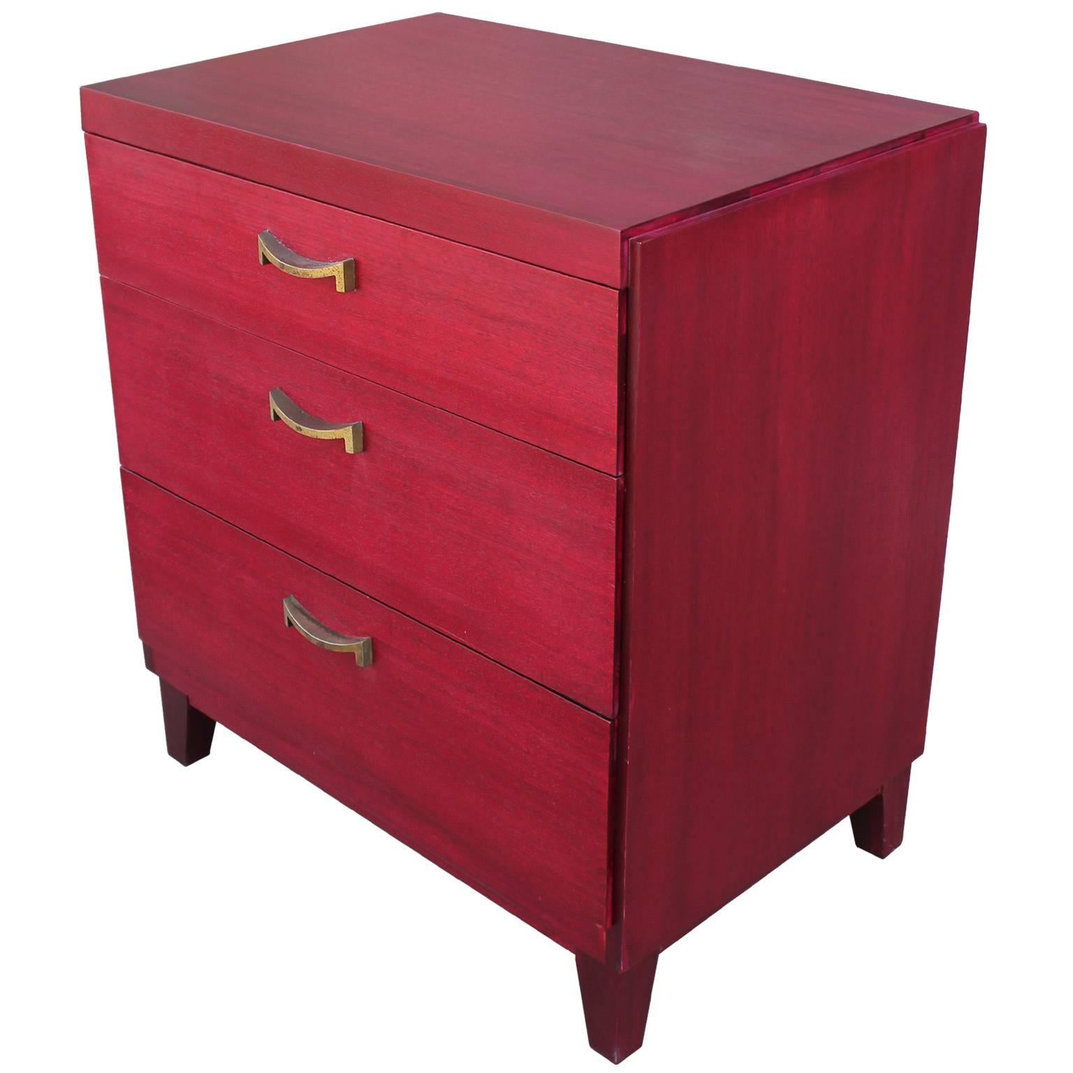 Striking bachelor's chest or small dresser. Dresser is finished in a lipstick red dye. Elegant brass hardware completes the piece. Three drawers provide storage. Perfect pop of color in a Hollywood Regency or transitional space.