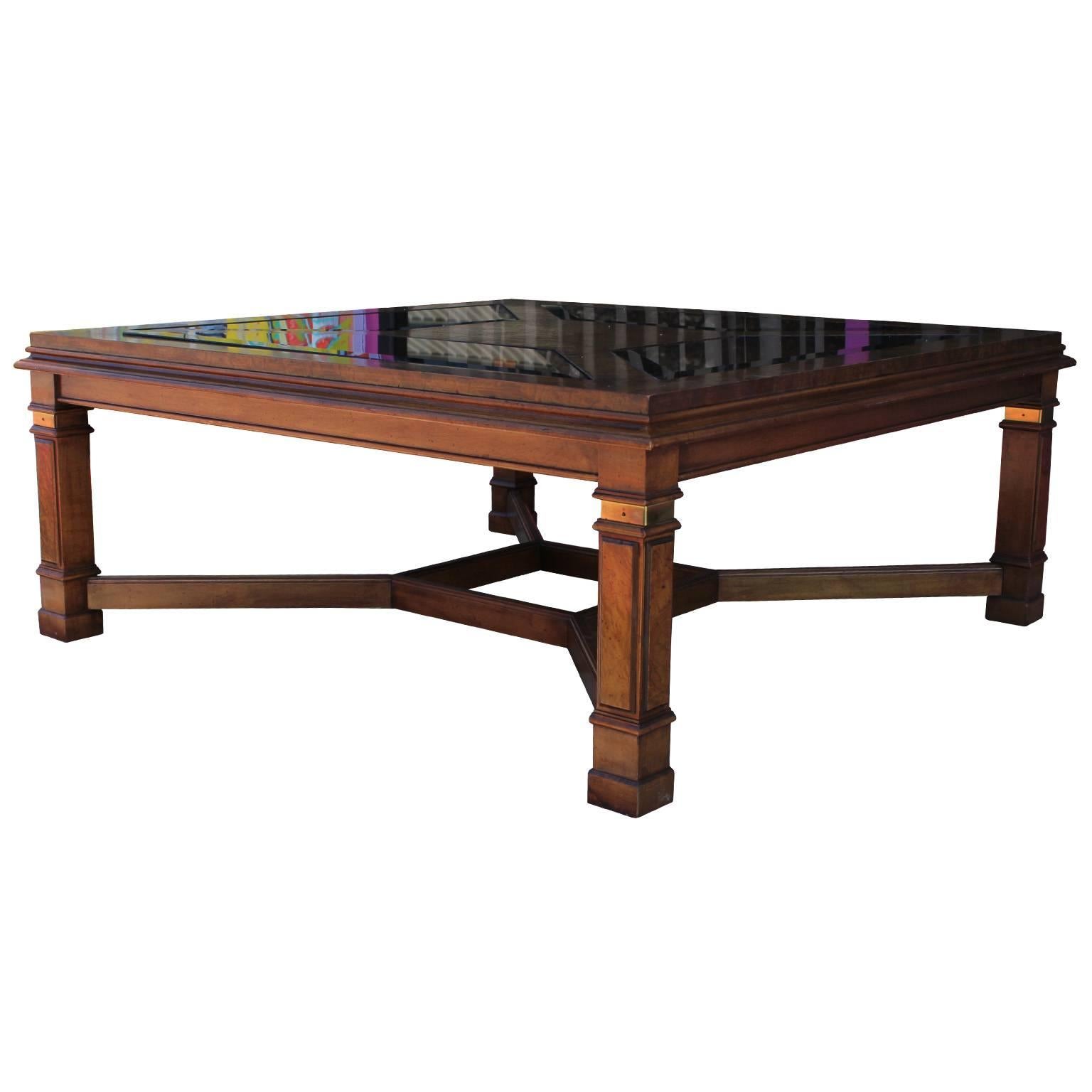 Elegant square coffee table. Tabletop is in burl wood with smoked glass panels. Panels mimic shape created by stretcher. Legs have brass band accents. Table has a wonderful attention to detail. Excellent in a traditional, Hollywood regency, or