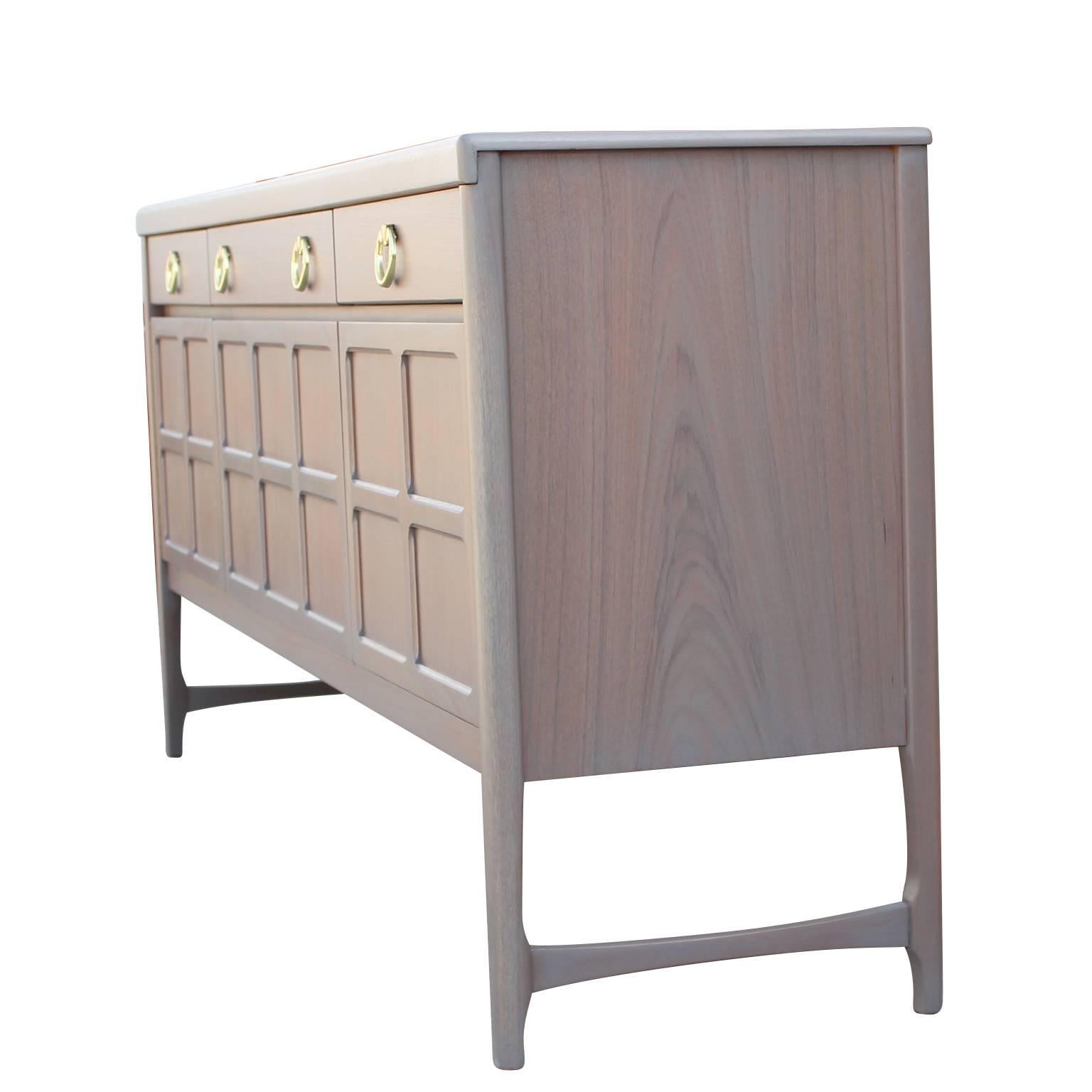 Modern Hollywood Regency sideboard richly refinished in a grey wash with a blush undertone and brass ring handles. This credenza features three drawers at the top; one with dividers, making it easy to keep organized and shelving on the bottom.