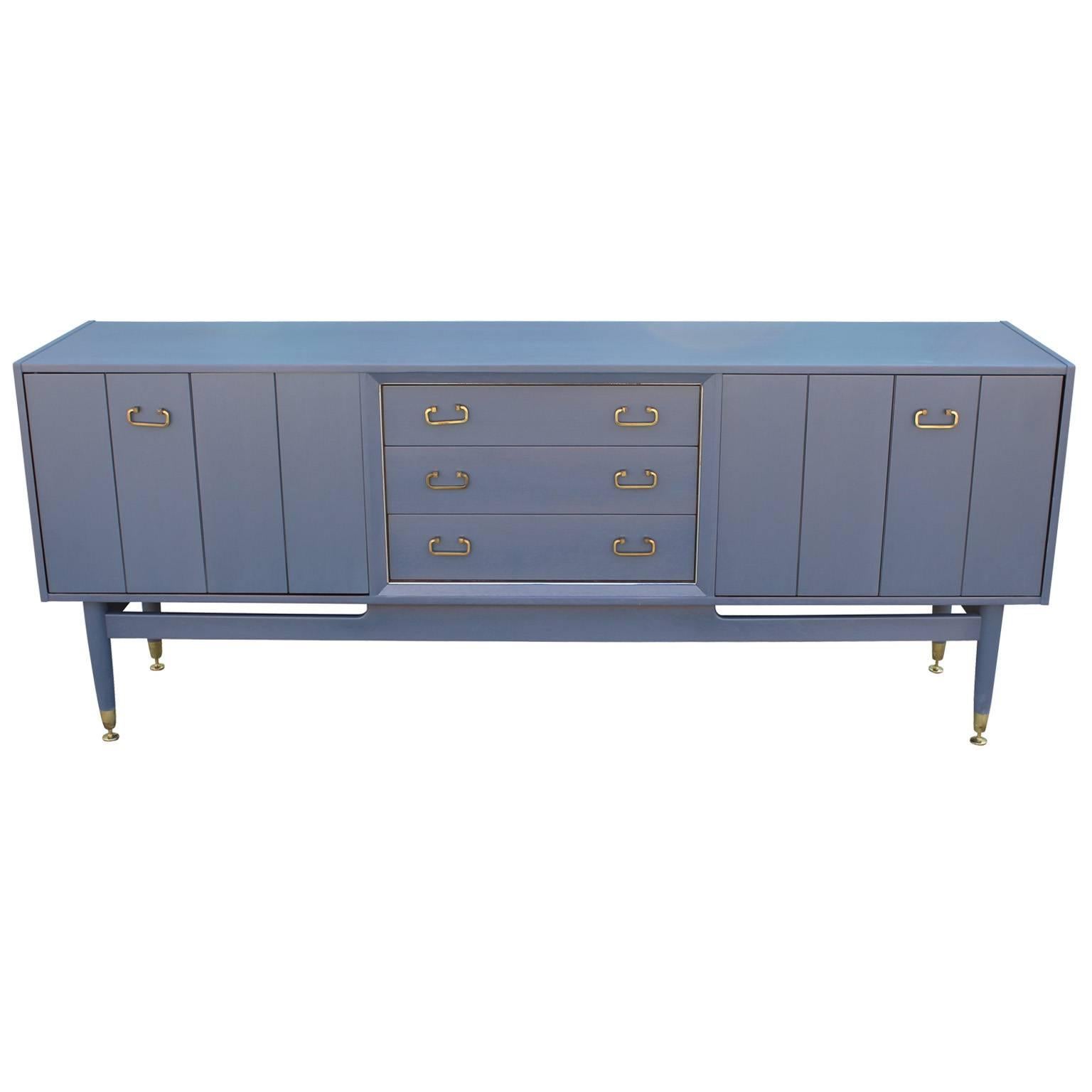 Sideboard or Credenza is made out of teak and has been stained a beautiful French Blue Grey.  Adjustable brass feet have been polished along with all hinges. Two folding doors open to a single shelf while three drawers provide additional storage.