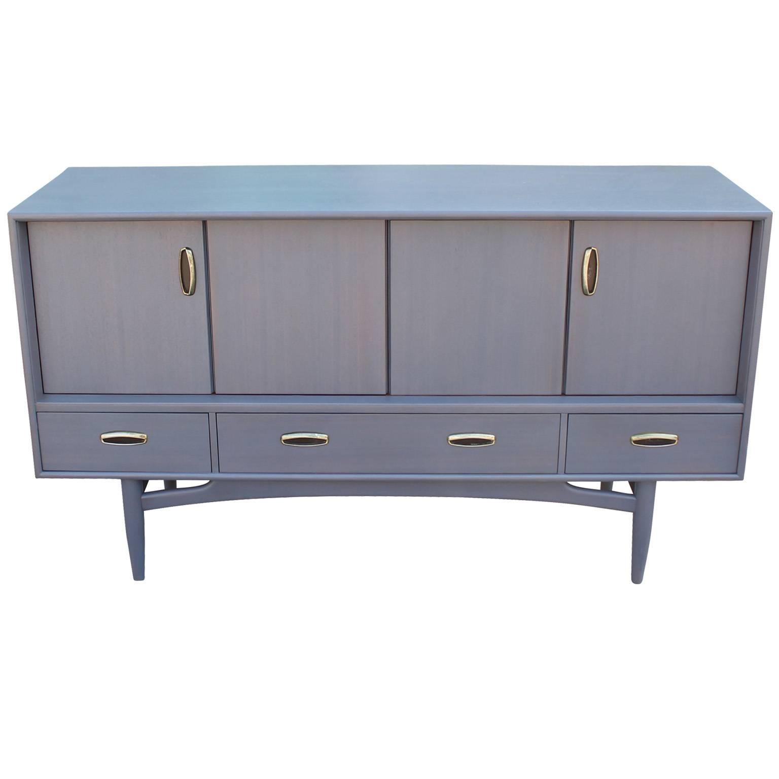 French grey-blue sideboard with aged brass handles. Sideboard or Credenza is made out of teak and is stained a beautiful pale French Blue Grey. Two folding door open to a single shelf. Three drawers provide additional storage.