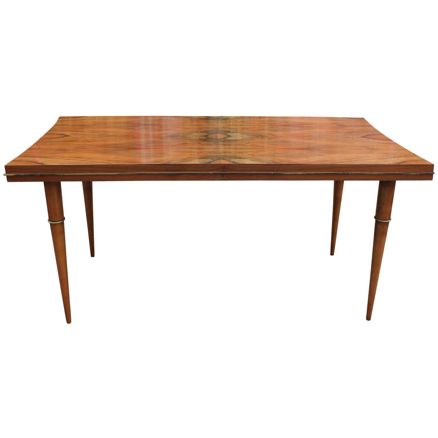 Stunning Italian dining table. Exotic table top have an incredible, lively grain. Brass accents trim the table top and add interest to the long tapered legs. Table top curves gently in on either end. Beautiful in a hollywood regency or transitional