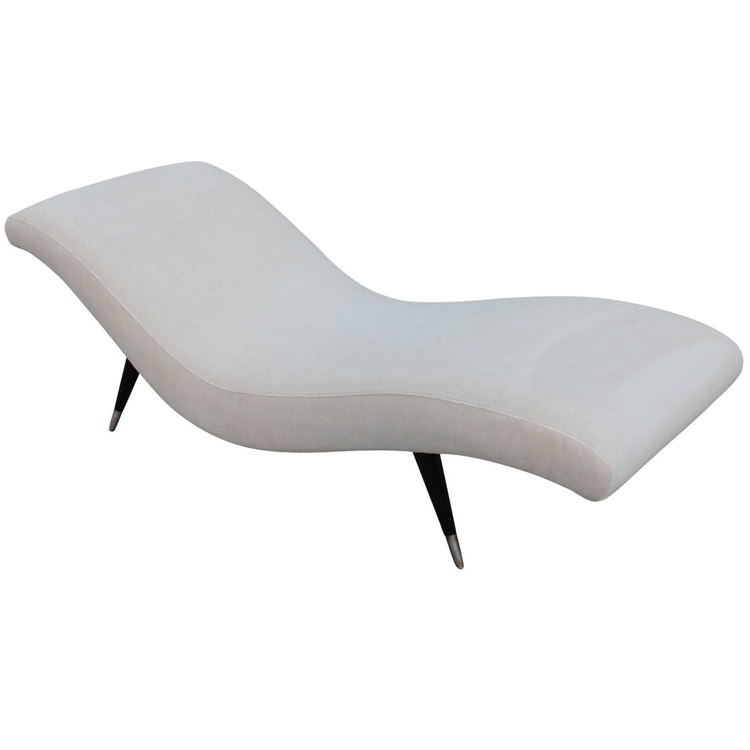 Stunning chaise lounge in cream color velvet. Chaise rests on four tapered and splayed legs in shiny black lacquer with heavily patinaed brushed metal caps. The swooping lines of the chaise are accentuated with delicate piping.  