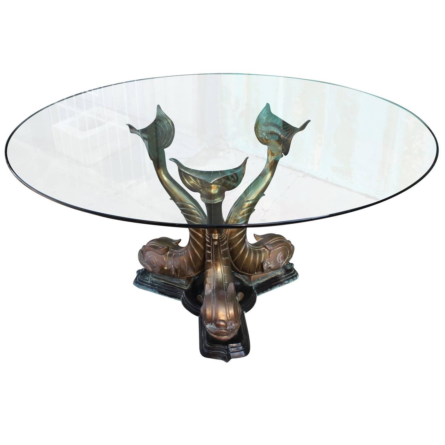 Incredible round dining table. Brass table base depicts three sculptural Dolphin fish. Topped with a thick glass, round top. The Table has a wonderful patina to it and is in excellent condition.