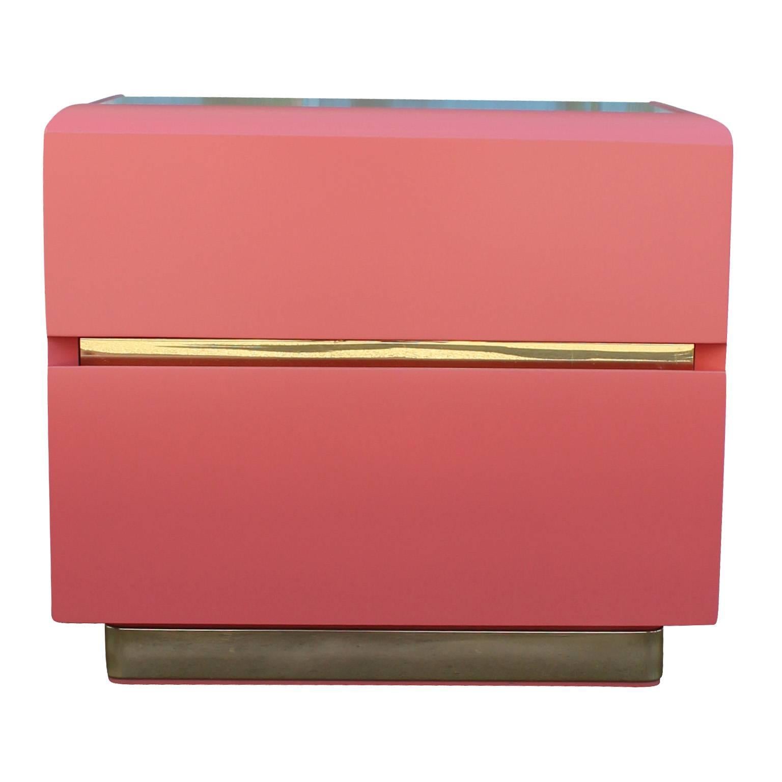 Ultra luxe pair of nightstands or end tables. Nightstands are freshly lacquered in a coral pink. Shiny brass adds visual interest to the bases and in between drawers. In excellent condition.