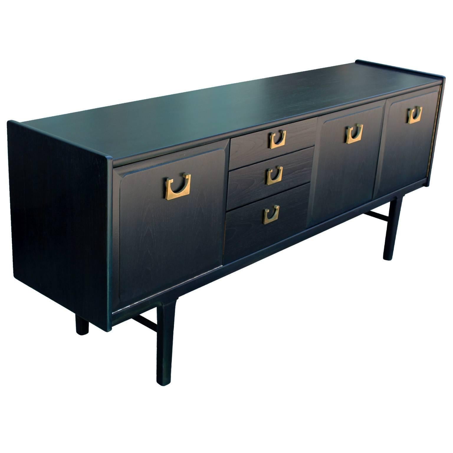 Striking sideboard freshly finished in a navy aniline dye. Sideboard has bold, brass hardware which nicely contrasts the stain. Drop down cabinet door on the left. Two cabinet drawers on the right reveal a single shelf. Three drawers provide