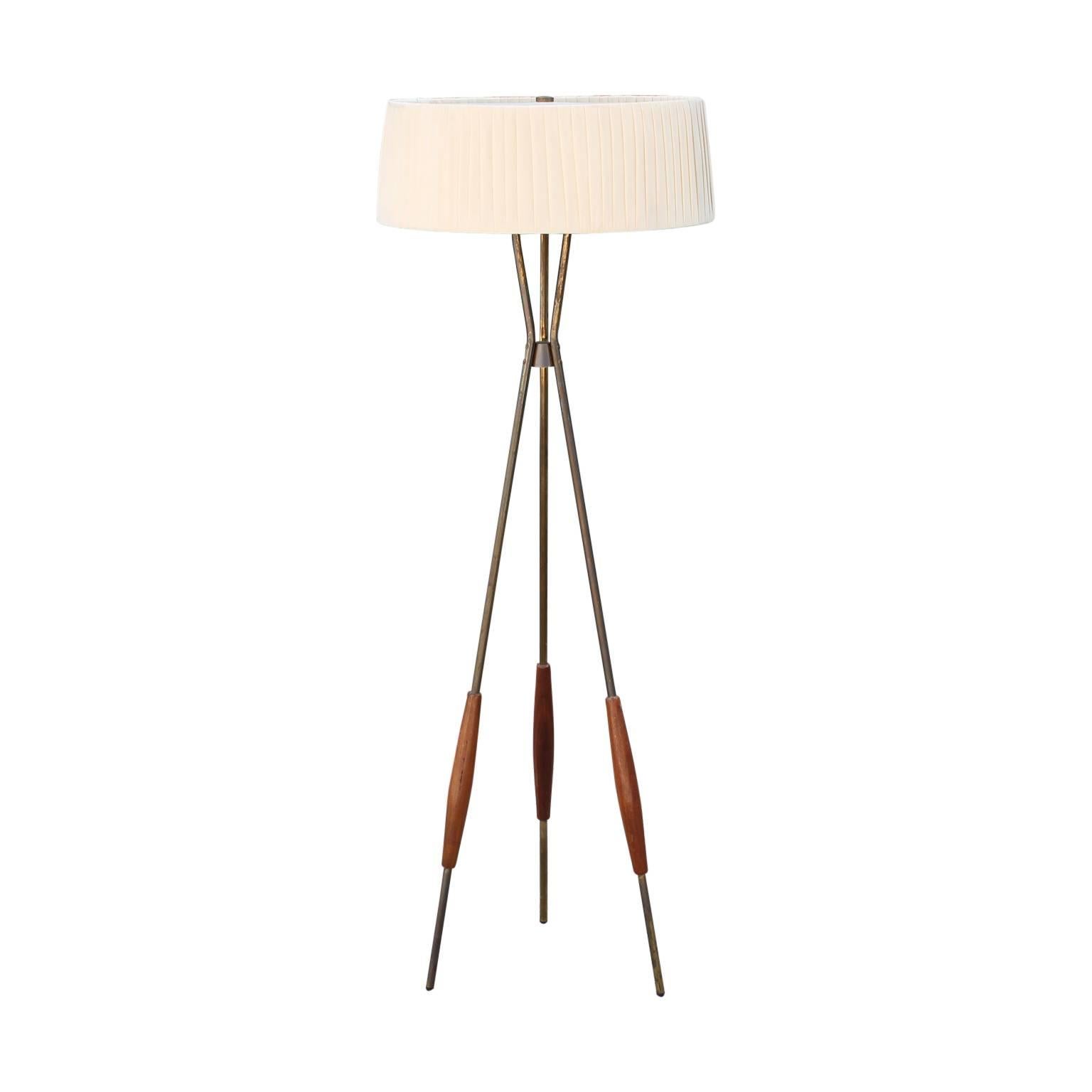 Mid-Century Modern tripod floor lamp by Gerald Thurston for Lightolier, circa 1950s. This piece features brass legs with solid walnut sleeves at the bottom of each leg and its original lampshade with a perforated metal diffuser and plastic bulb