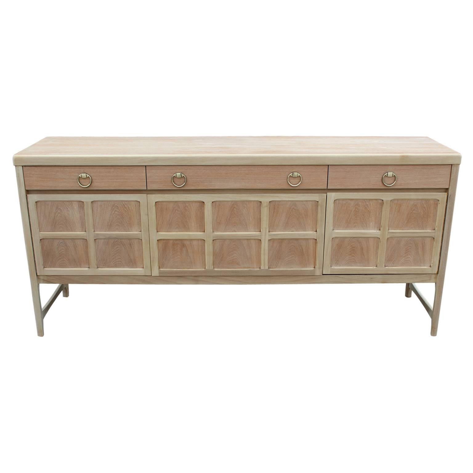 Freshly bleached sophisticated sideboard with brass ring handles. Center cabinet drops down. Three drawers provide additional storage.