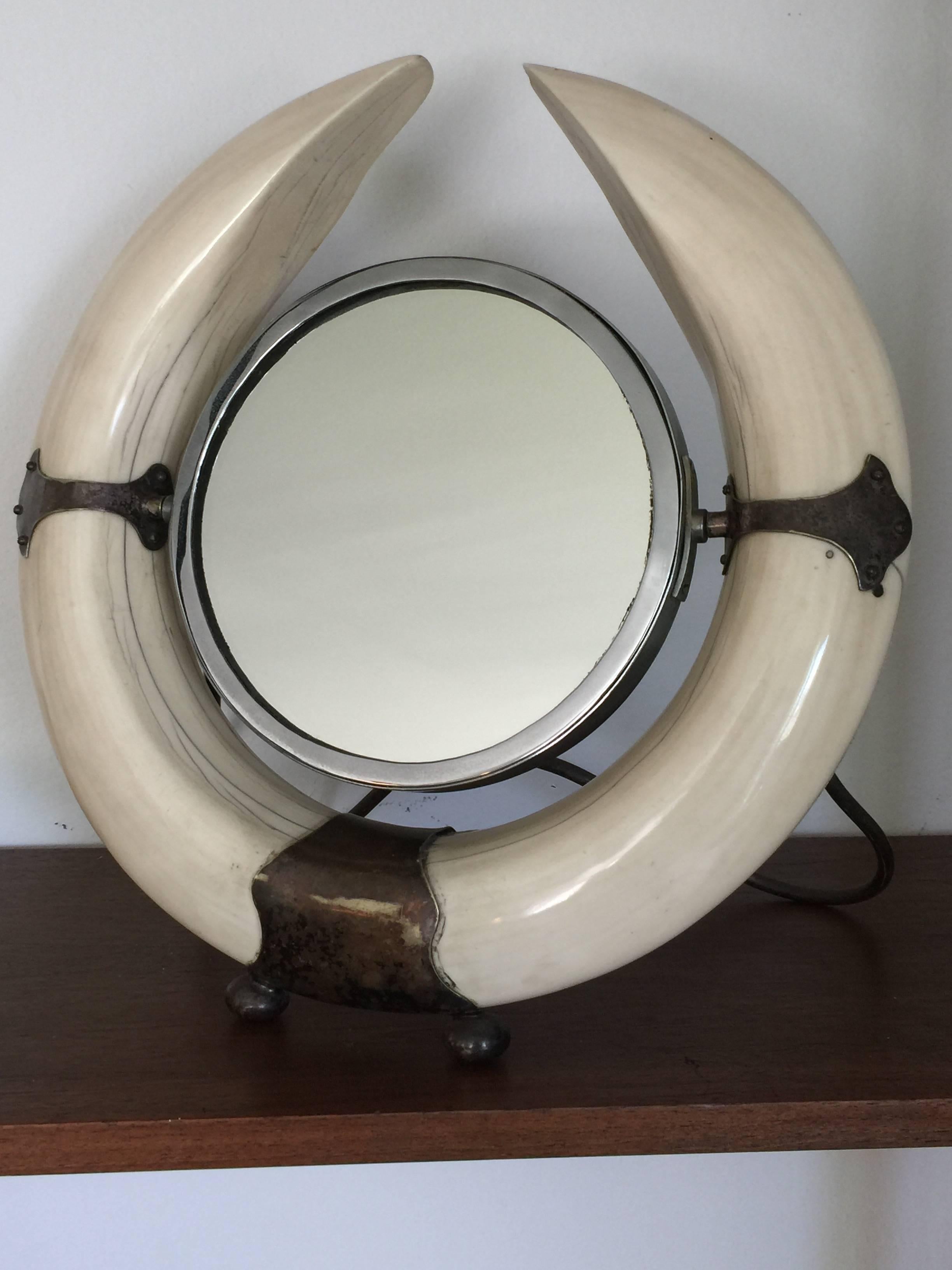 A silver plate mounted walrus tusk dressing mirror,

circa 1880. 

The circular plate with a pierced cresting flanked by tusk.