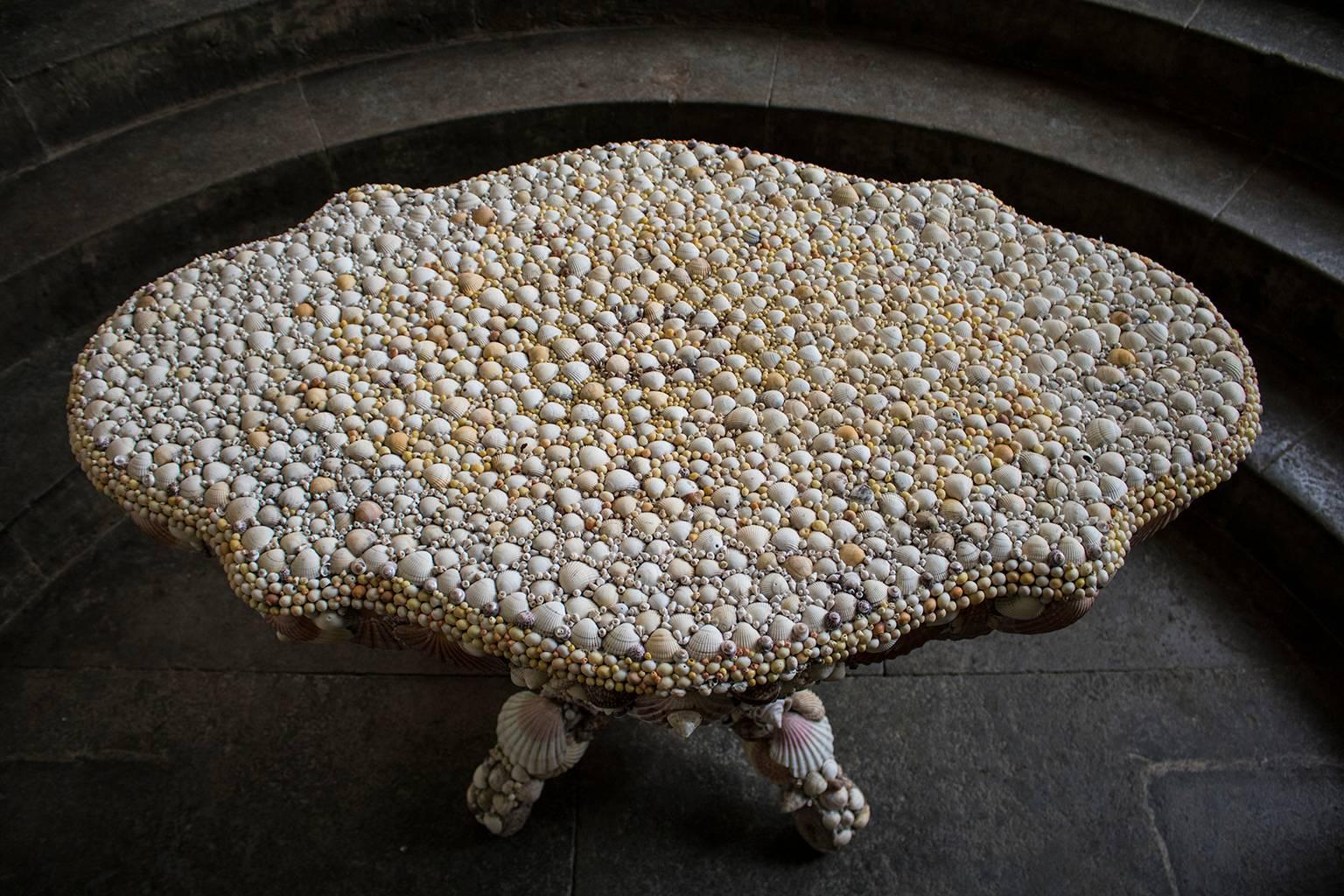 A shellwork centre table by Antony Redmile, circa 1970s. The central support raised on four splayed feet, the shaped top and body encrusted throughout with cowrie, scallop and clam shells.

Please enquire about international shipping costs.