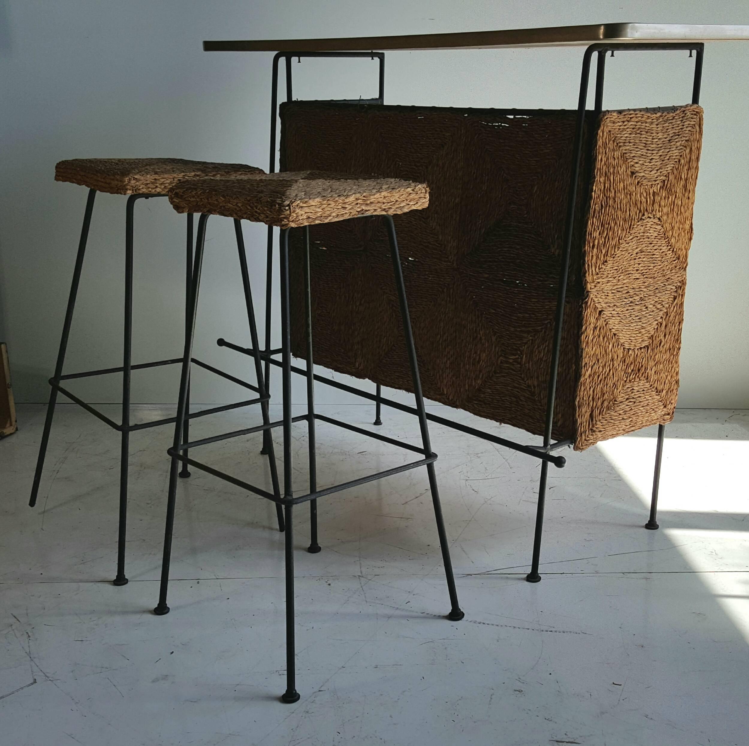 Classic Mid-Century Modern bar/stools designed by Arthur Umanoff, iron and laminate construction as well as natural fiber weaved panels and slat wood shelves, included two original iron and natural fiber bar stools, (one stool missing feet caps)