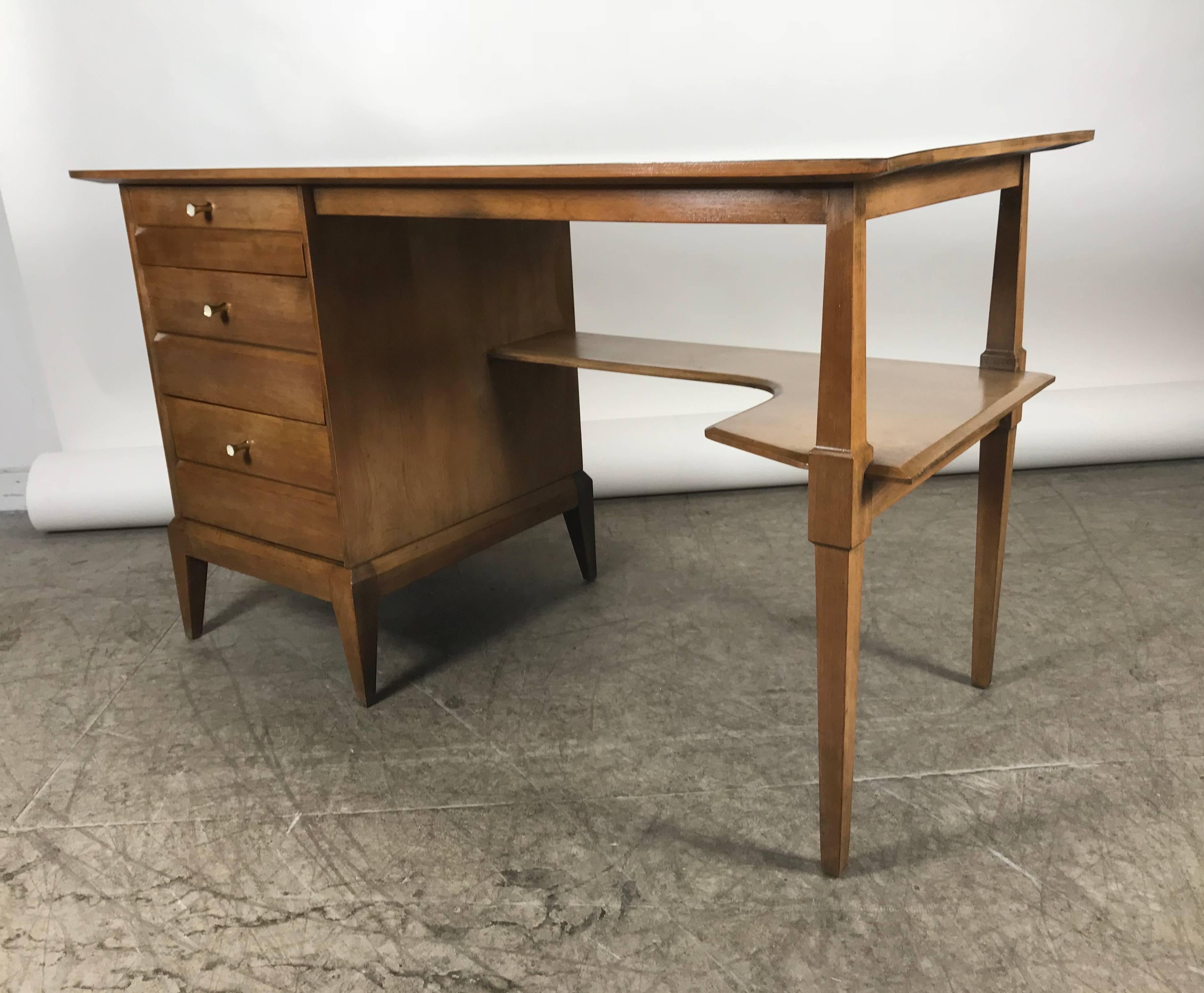 Stylized Mid-Century Modern desk by Heywood Wakefield, warm walnut finish, white laminate top, featuring three drawers and right lower shelf, stylized conical brass drawer pulls, finished back, superior quality and construction.