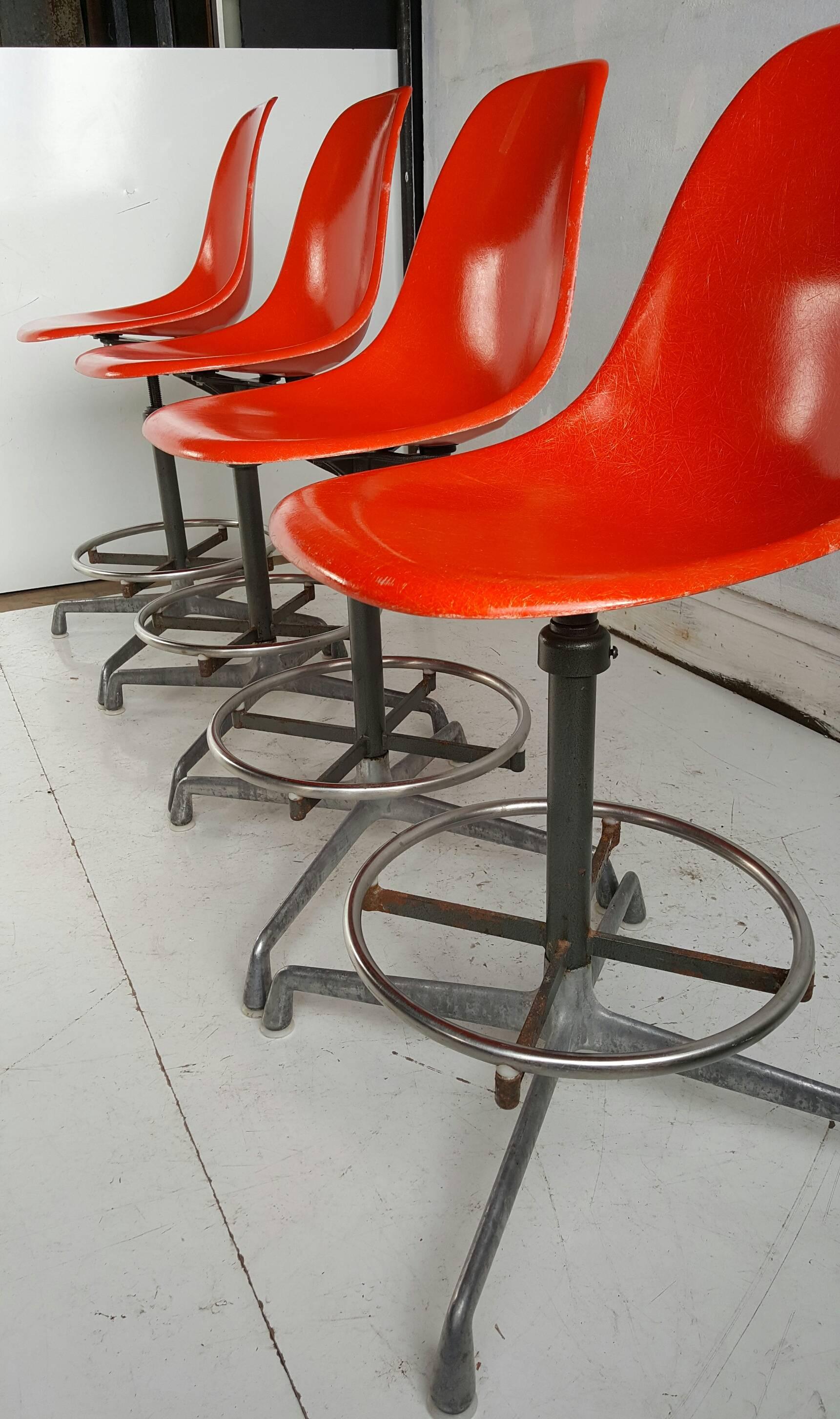 Nice set of four matching architectural adjustable drafting stool having a molded fiberglass seat and round foot rest floating on a four pronged cast aluminum base.