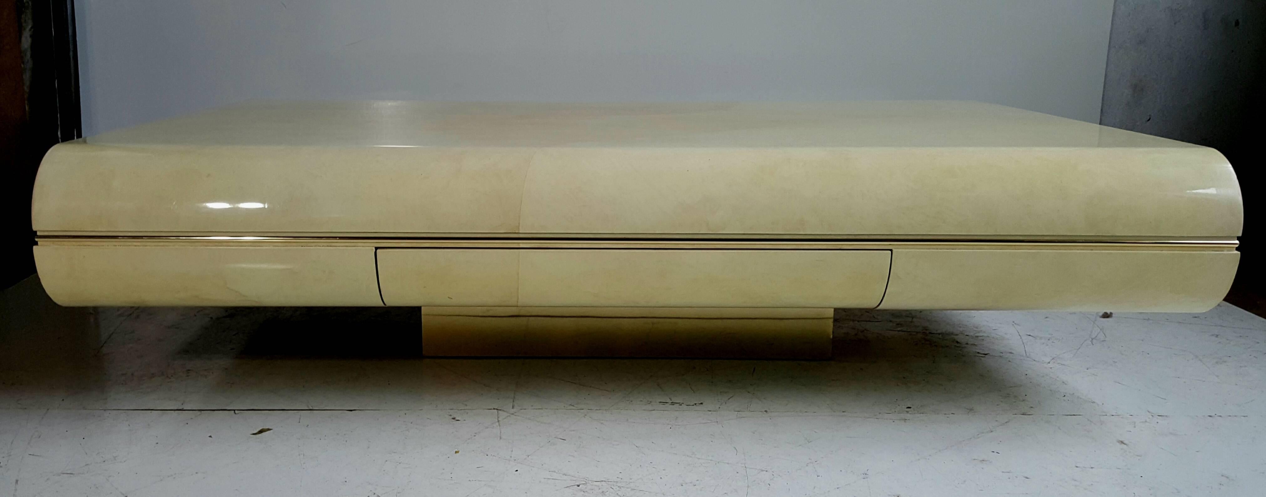 Large faux goatskin covered cocktail table. Stunning design, low profile. Floating table sits on brass wrapped square plinth. Hidden single drawer detail, nice brass detail trim wrap around. Measures: 60
