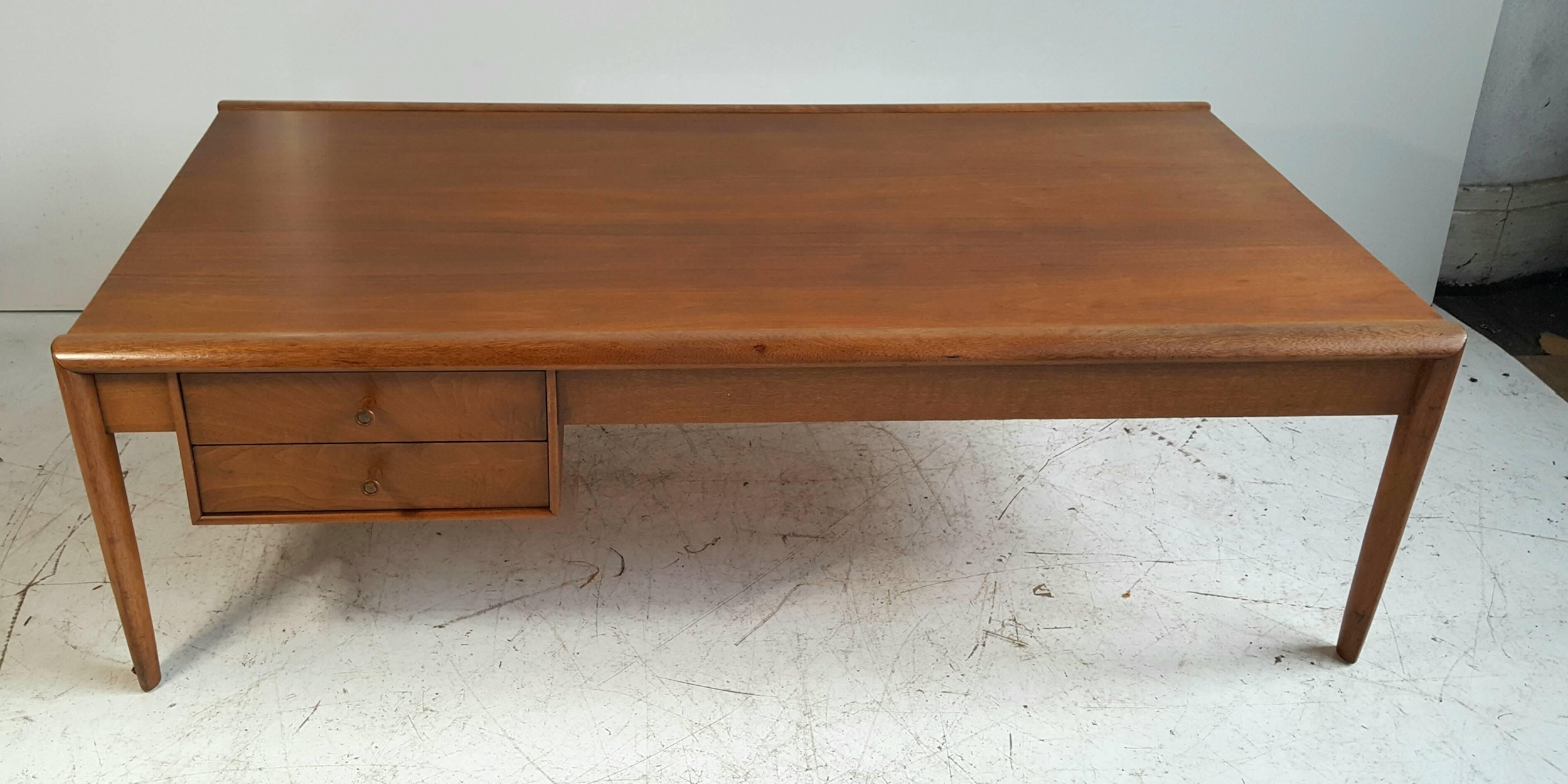 Classic Mid-Century Modern cocktail or coffee table... reminiscent of classic designs from T. H. Robsjohn Gibbings... Wonderful warm blonde mahogany wood... featuring two drawers... and generous top surface... Classic tapered leg and surround detail.